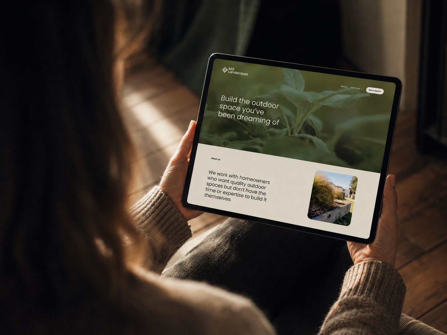 Person holding a tablet showing a website for Mill Landscapes, with the headline "Build the outdoor space you’ve been dreaming of" and a photo of a landscaped yard.