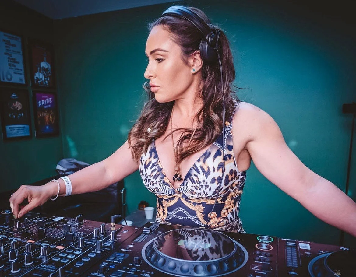A female DJ wearing headphones, mixing music on a professional DJ controller in a club or studio setting.
