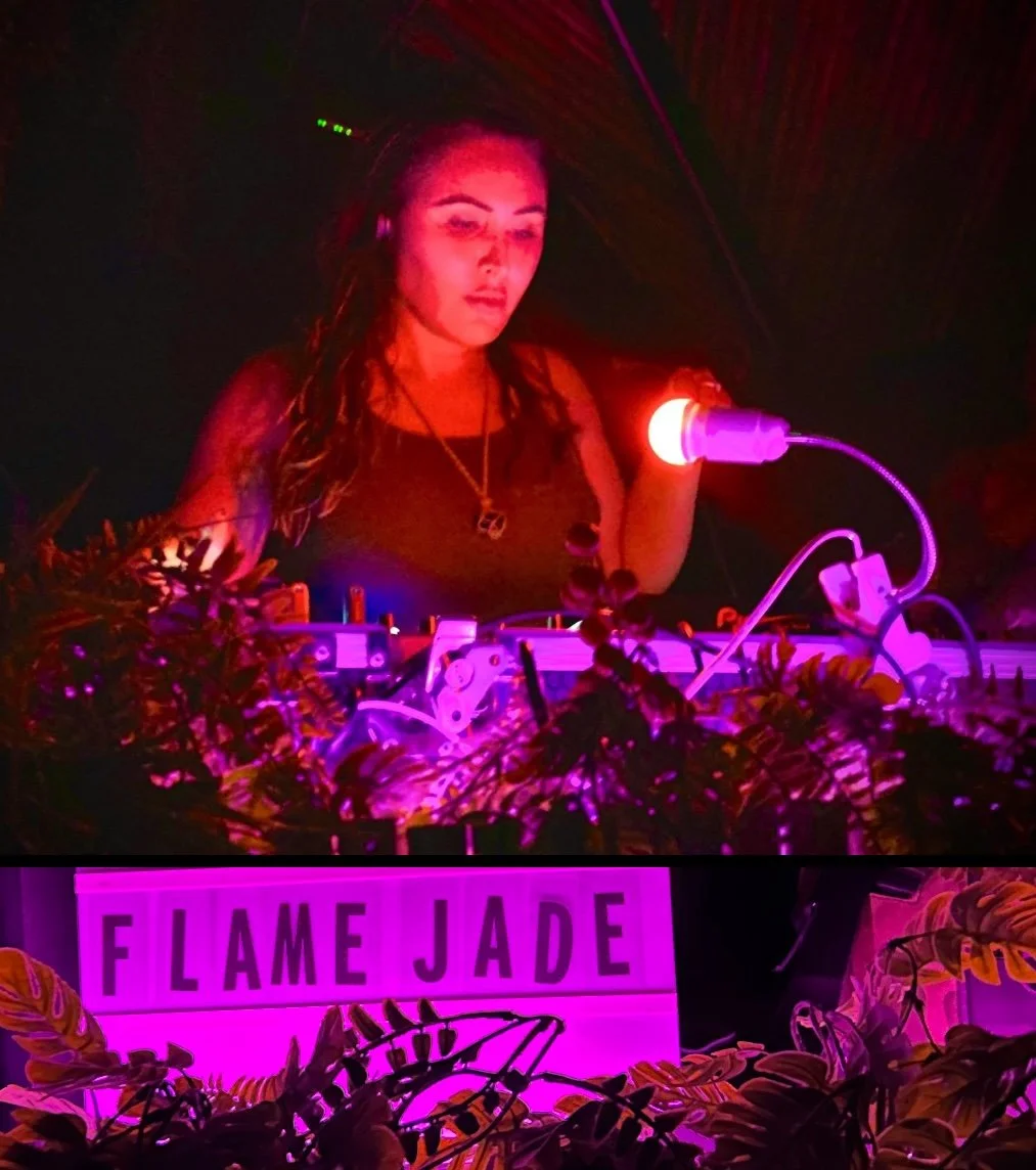 A female DJ standing behind a DJ setup with colorful lights, plants, and a sign that says 'F I L A M E J A D E' underneath.