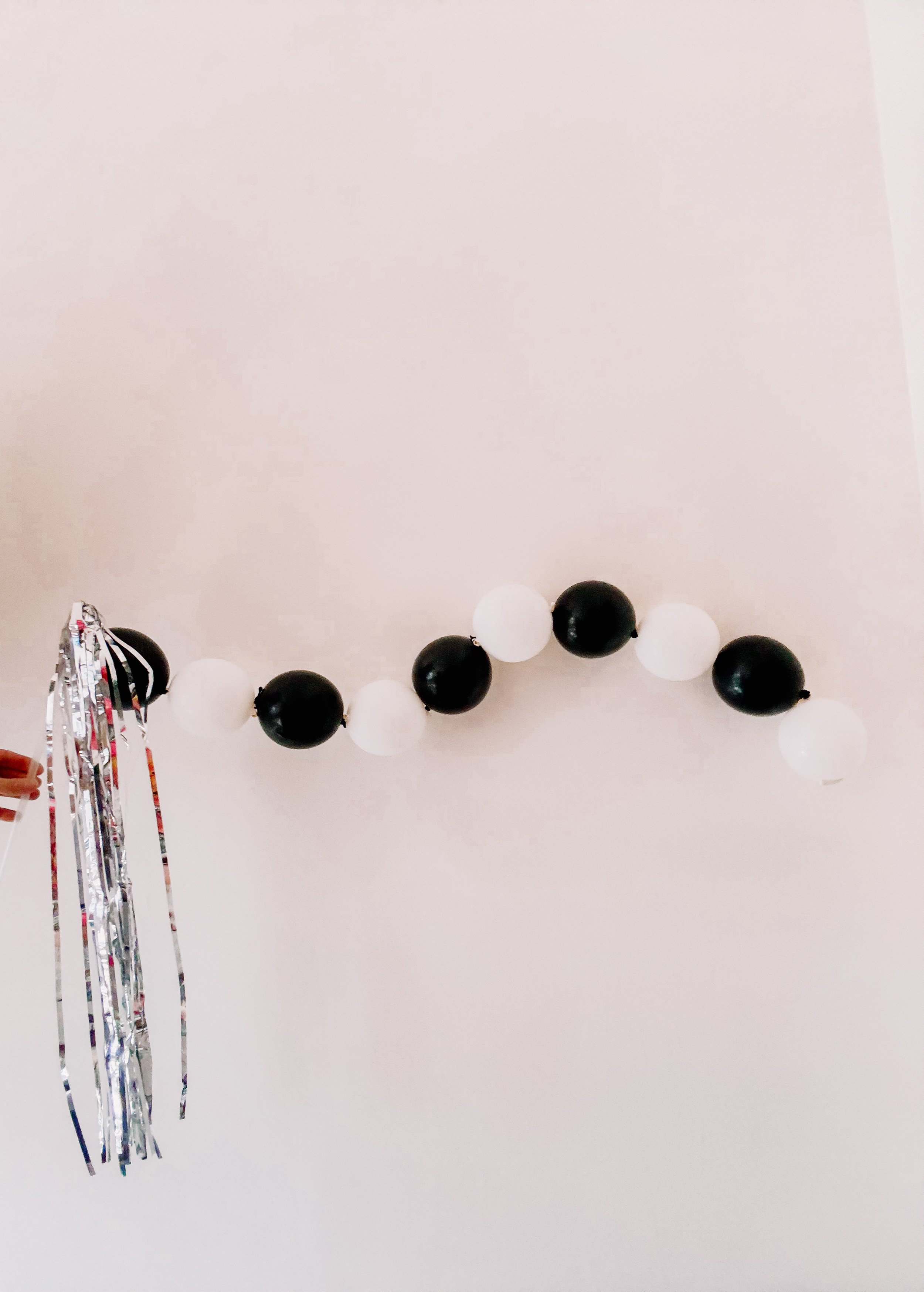 Black and white balloon wand with long metallic silver tinsel fringe, handheld New Year’s party favor for kids and adults.