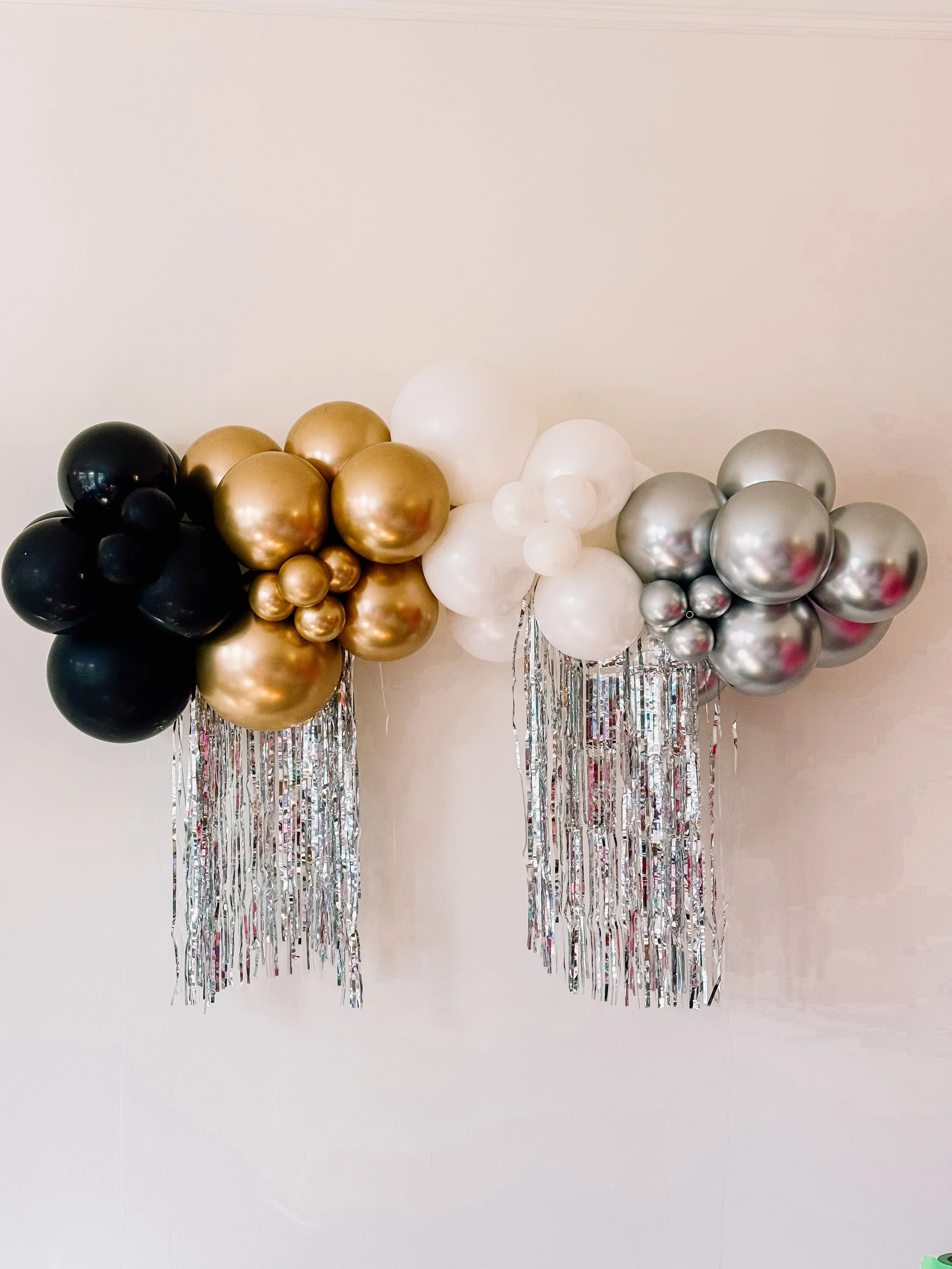 New Year’s Eve 5-foot balloon garland in black, gold, white, and silver balloons with metallic silver hanging tinsel, luxury party décor installation.