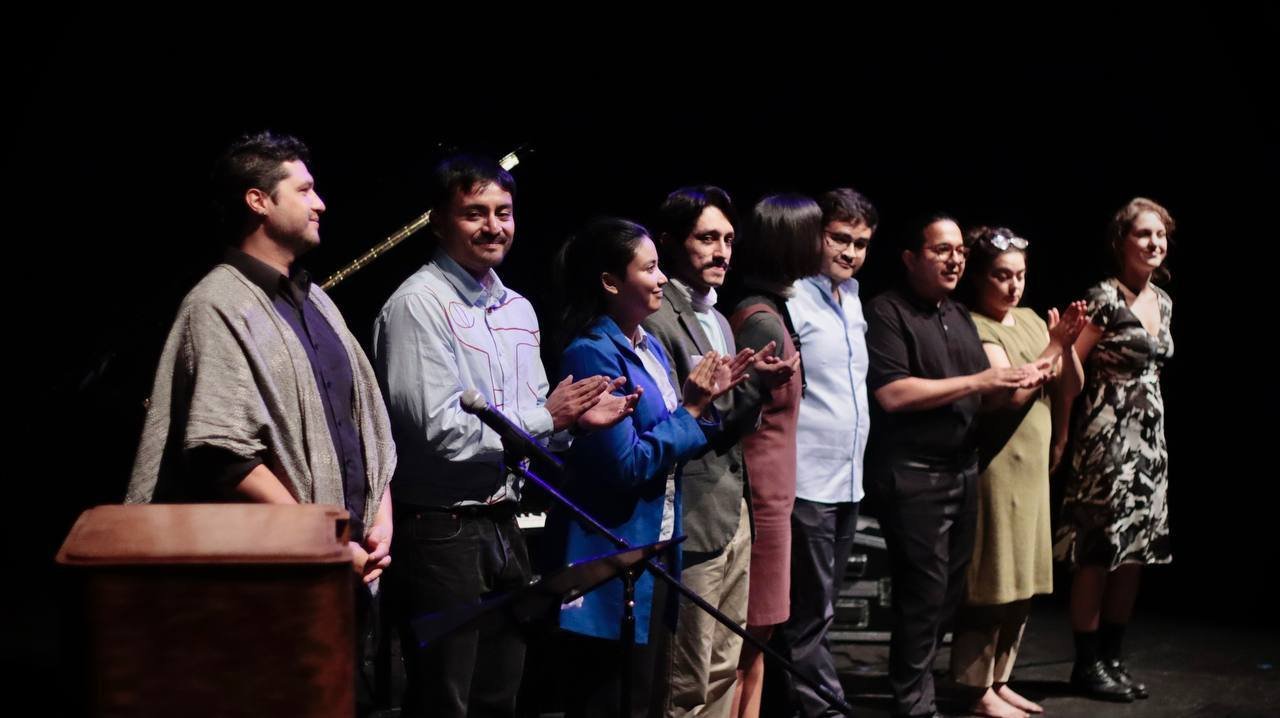 Grupo de personas en un escenario aplaudiendo, posiblemente en un evento o presentación.
