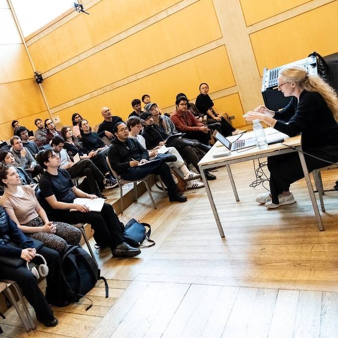 Grupo de personas asistiendo a una conferencia en un auditorio, con una mujer en el podio presentando.
