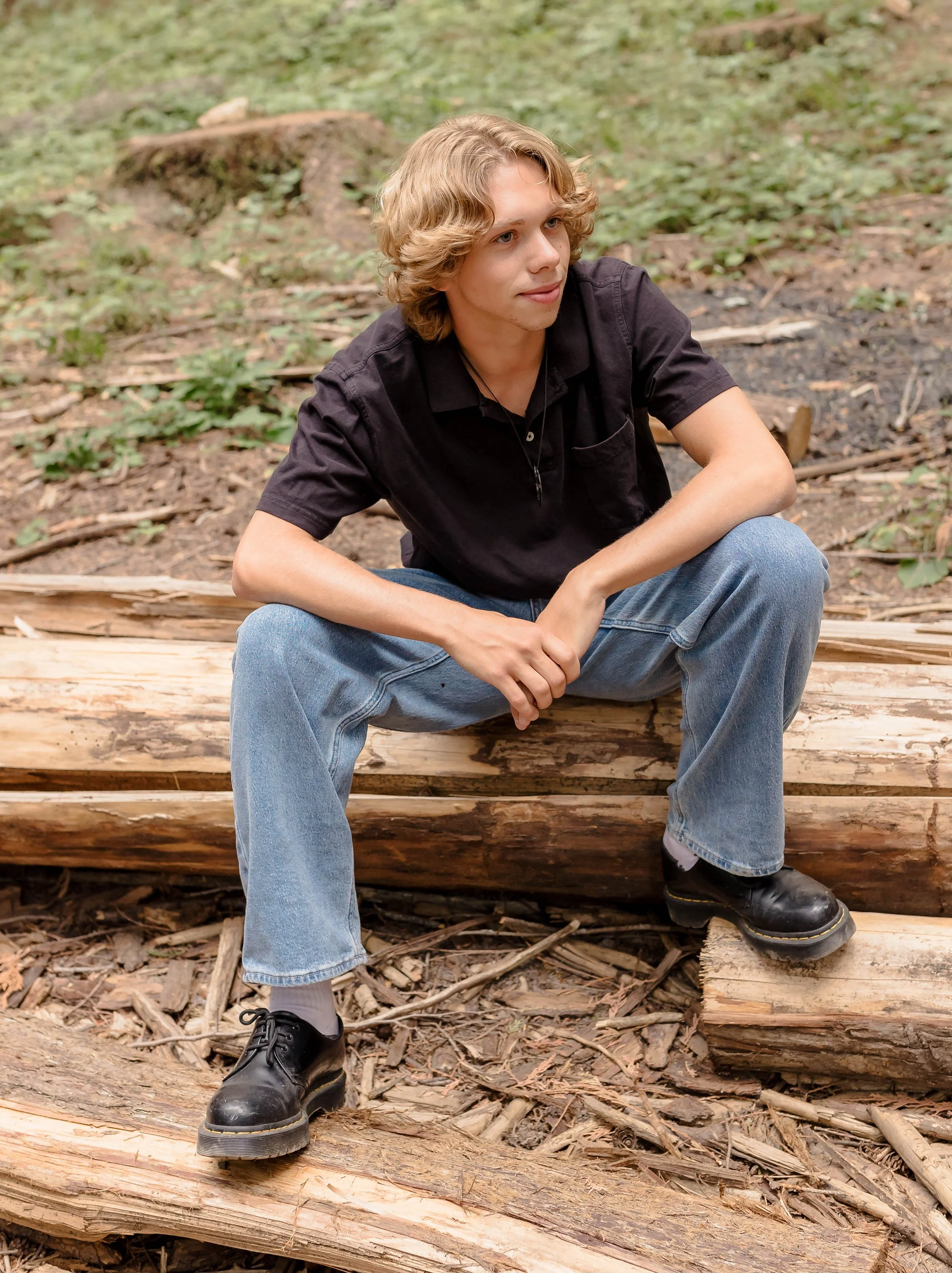 Senior boy poses on a fallen tree in the woods.
