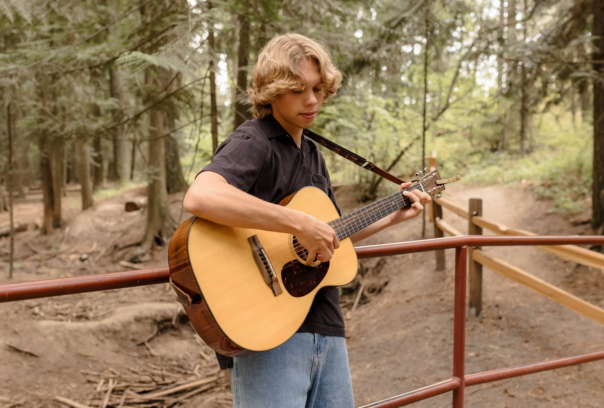 Teen boy plays his guitar in the woods.