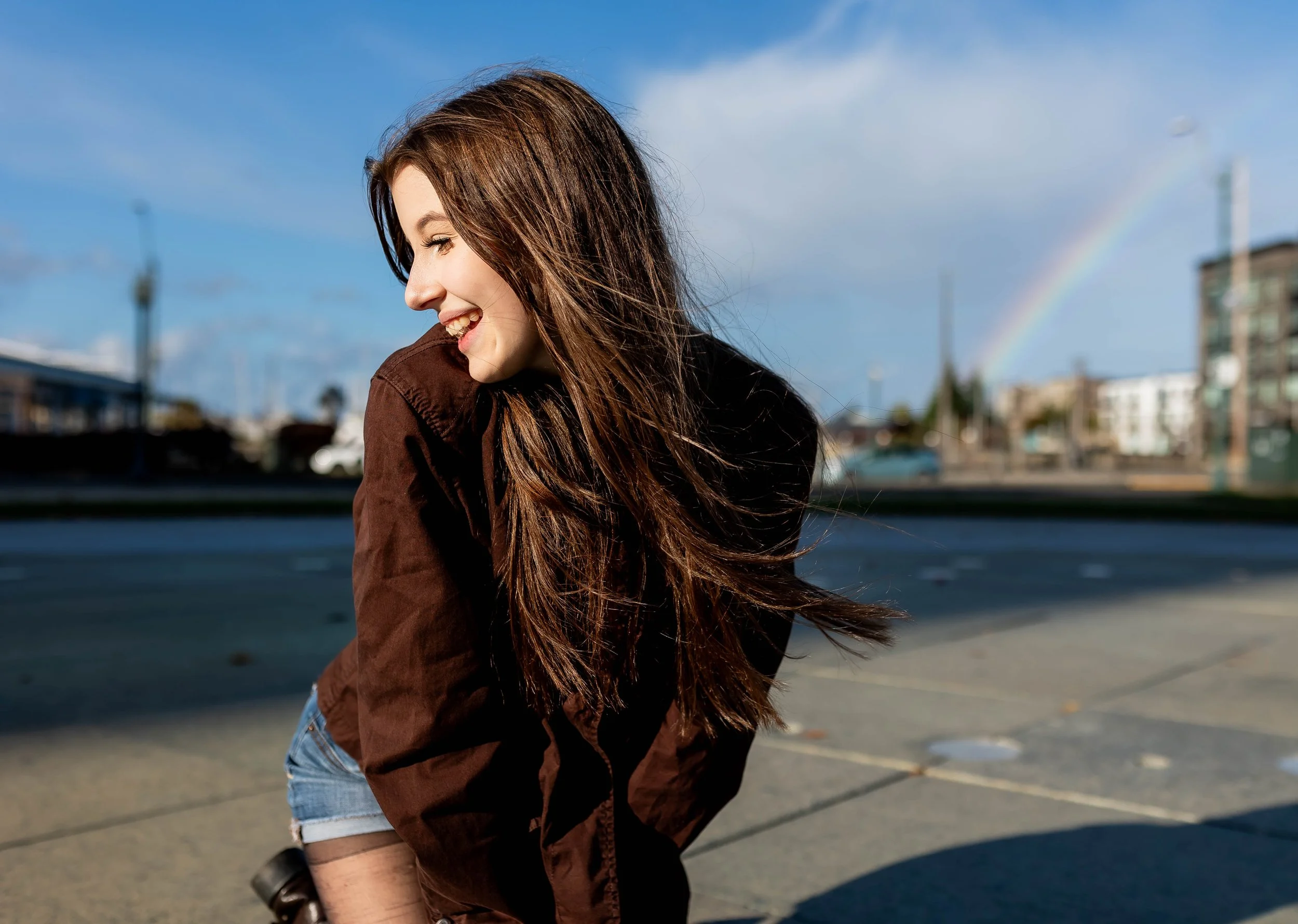 Senior girl smiling over shoulder downtown Olympia with a rainbow in the sky.