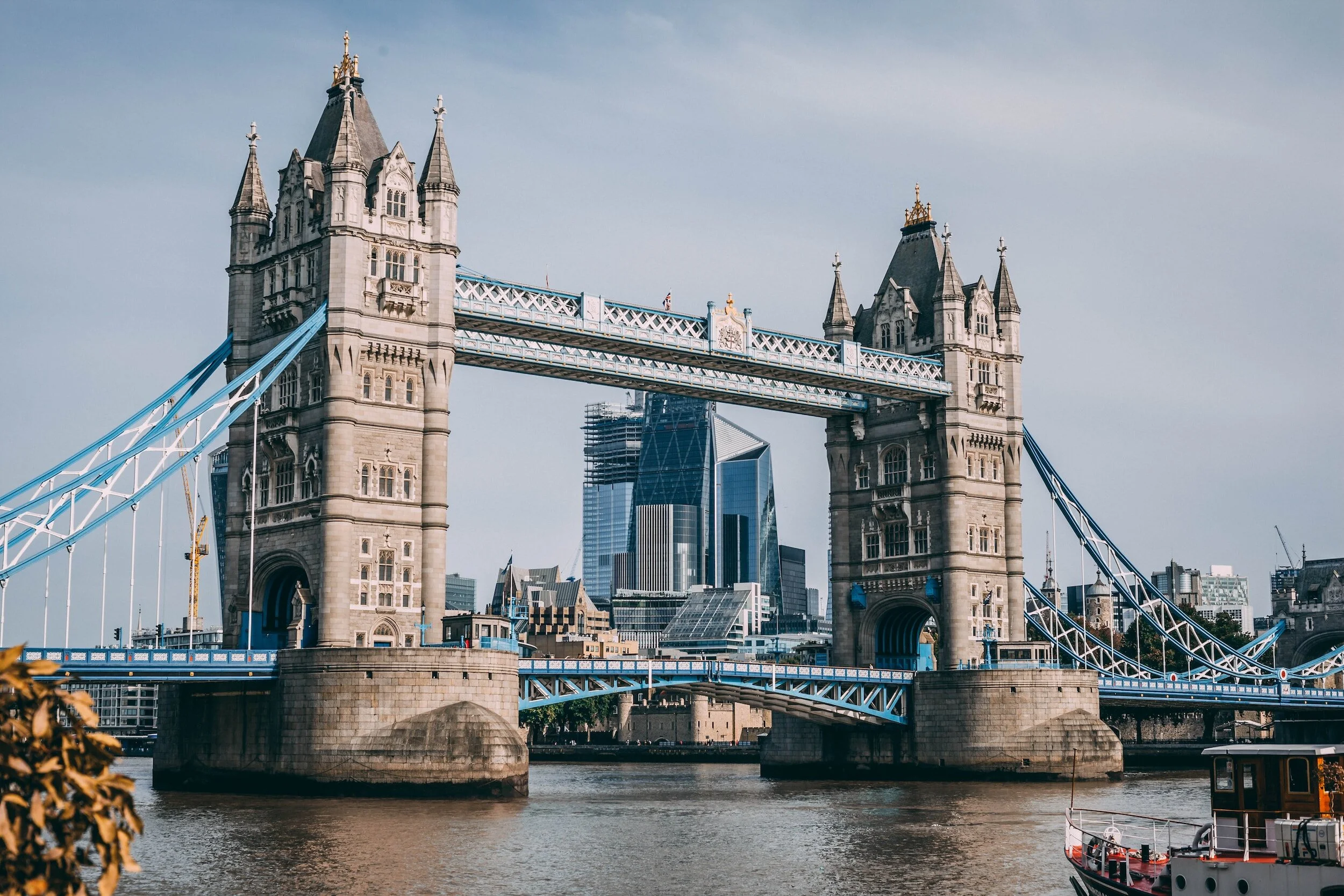 London's Tower Bridge spanning the River Thames with modern skyscrapers in the background under a partly cloudy sky.