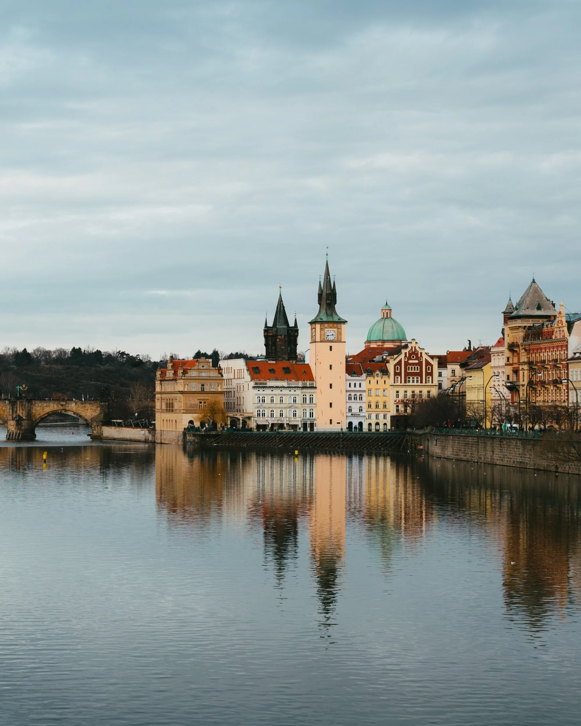 View of old European city skyline with historic buildings and a river in the foreground reflecting the cityscape.