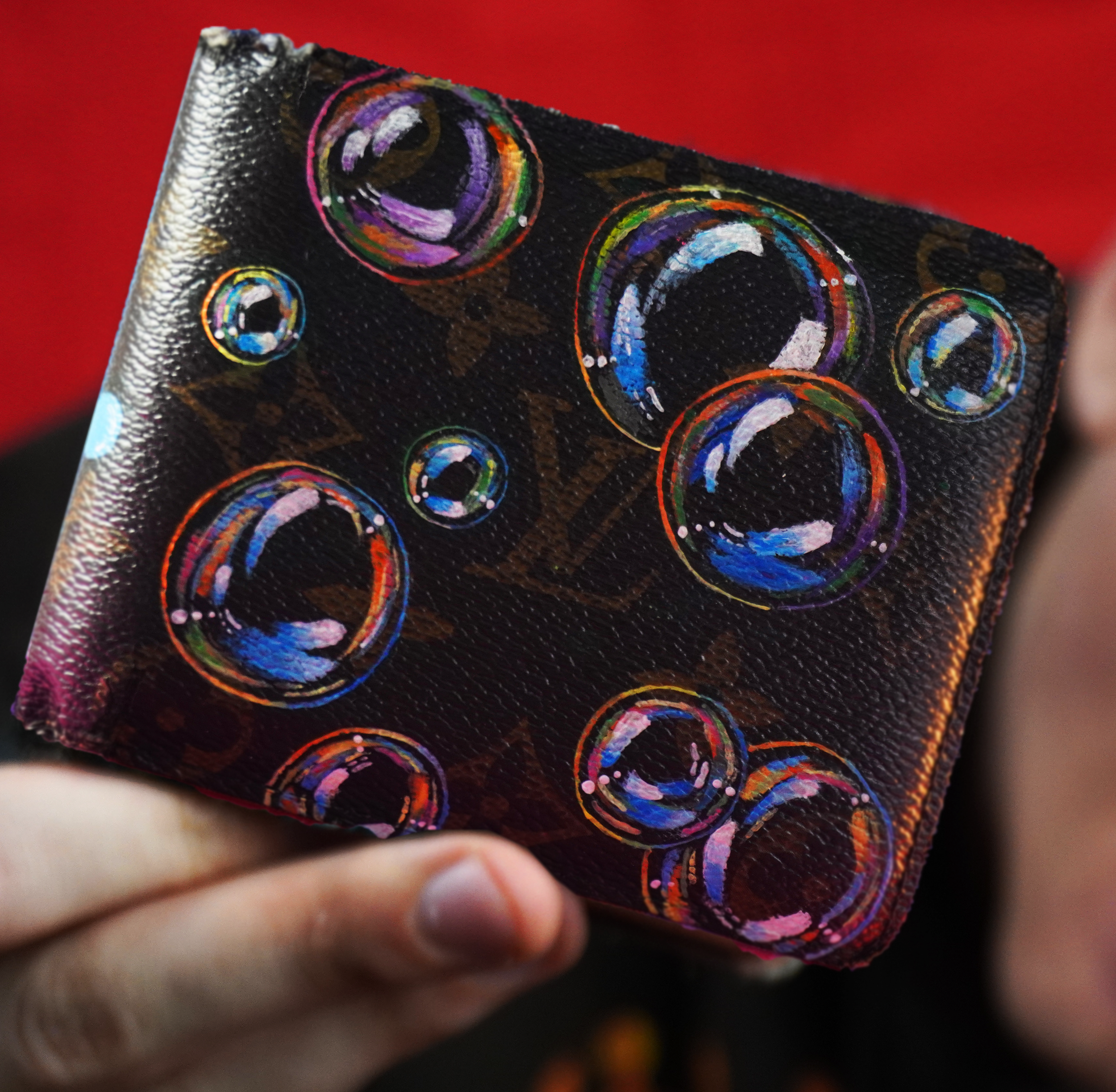 Hand holding a dark leather wallet with colorful bubble designs against a red background.