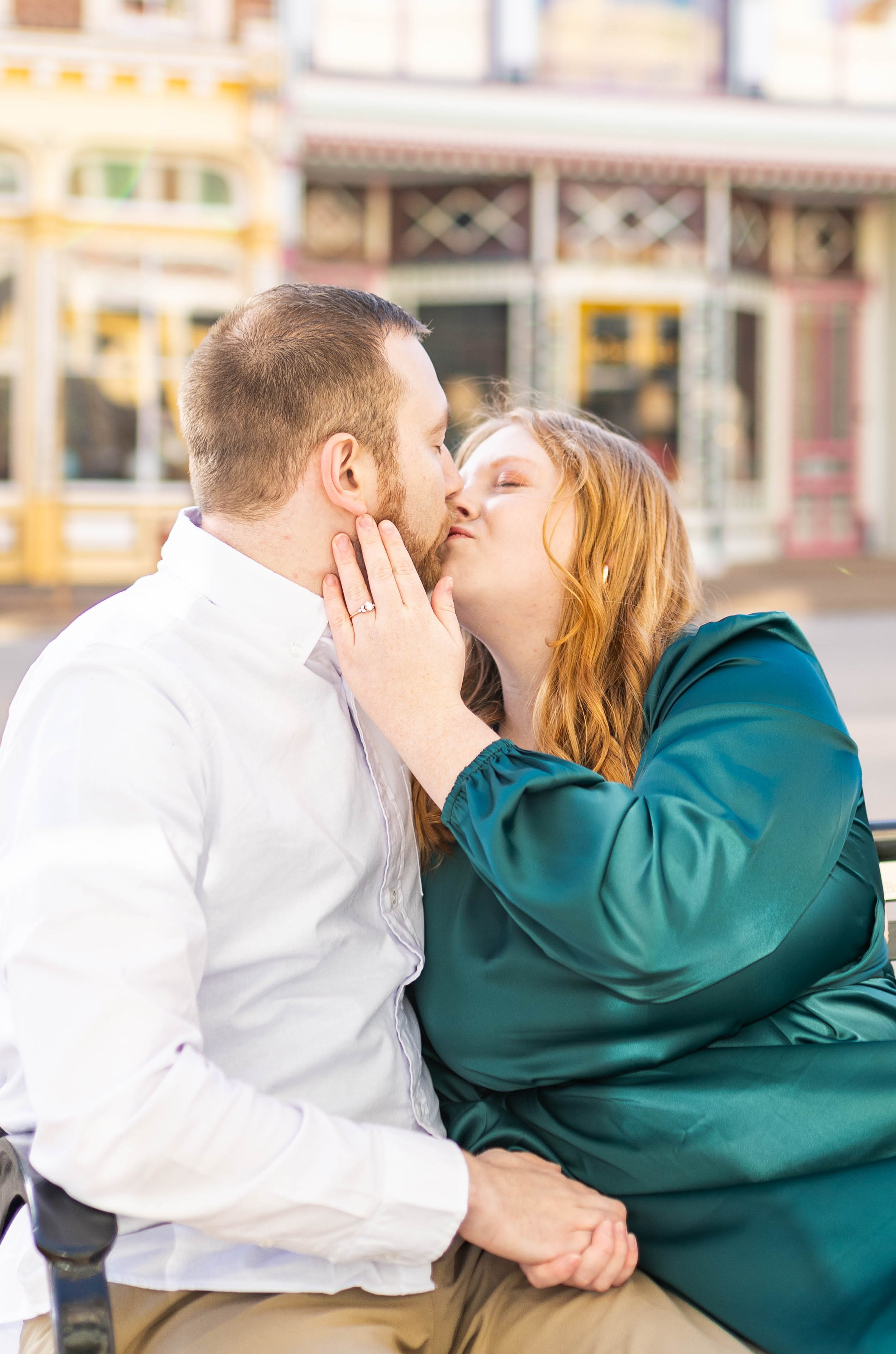 A couple sharing a kiss outdoors in front of colorful storefronts on a city street.