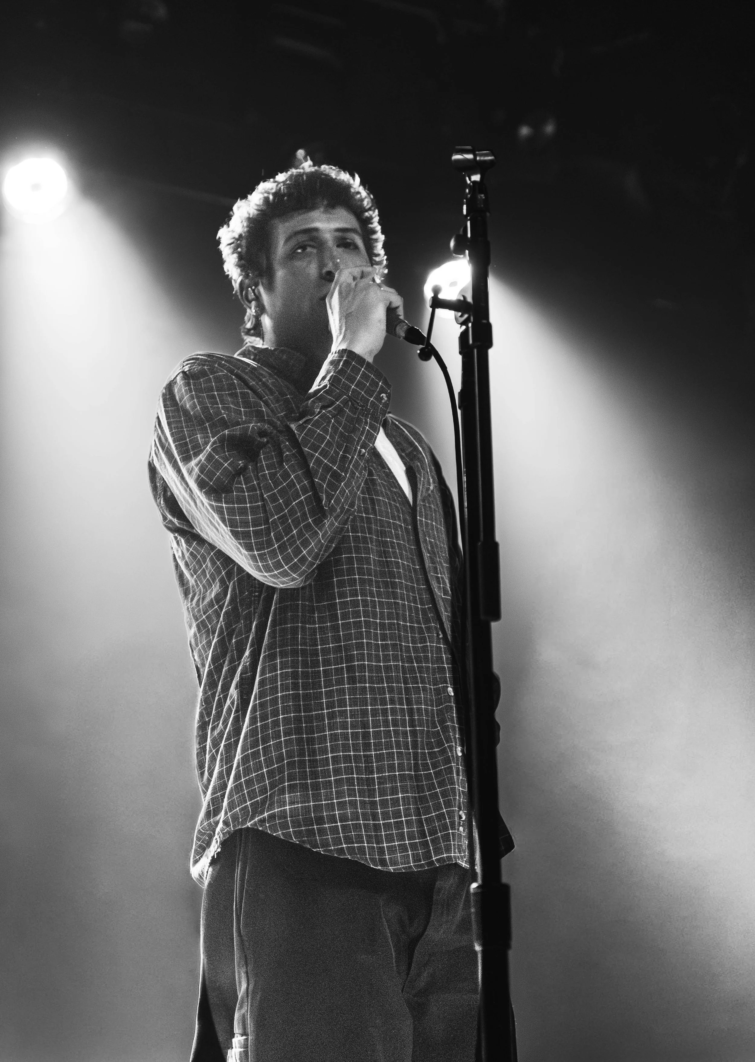Black and white photo of a young person singing into a microphone on a stage with bright lights behind them.