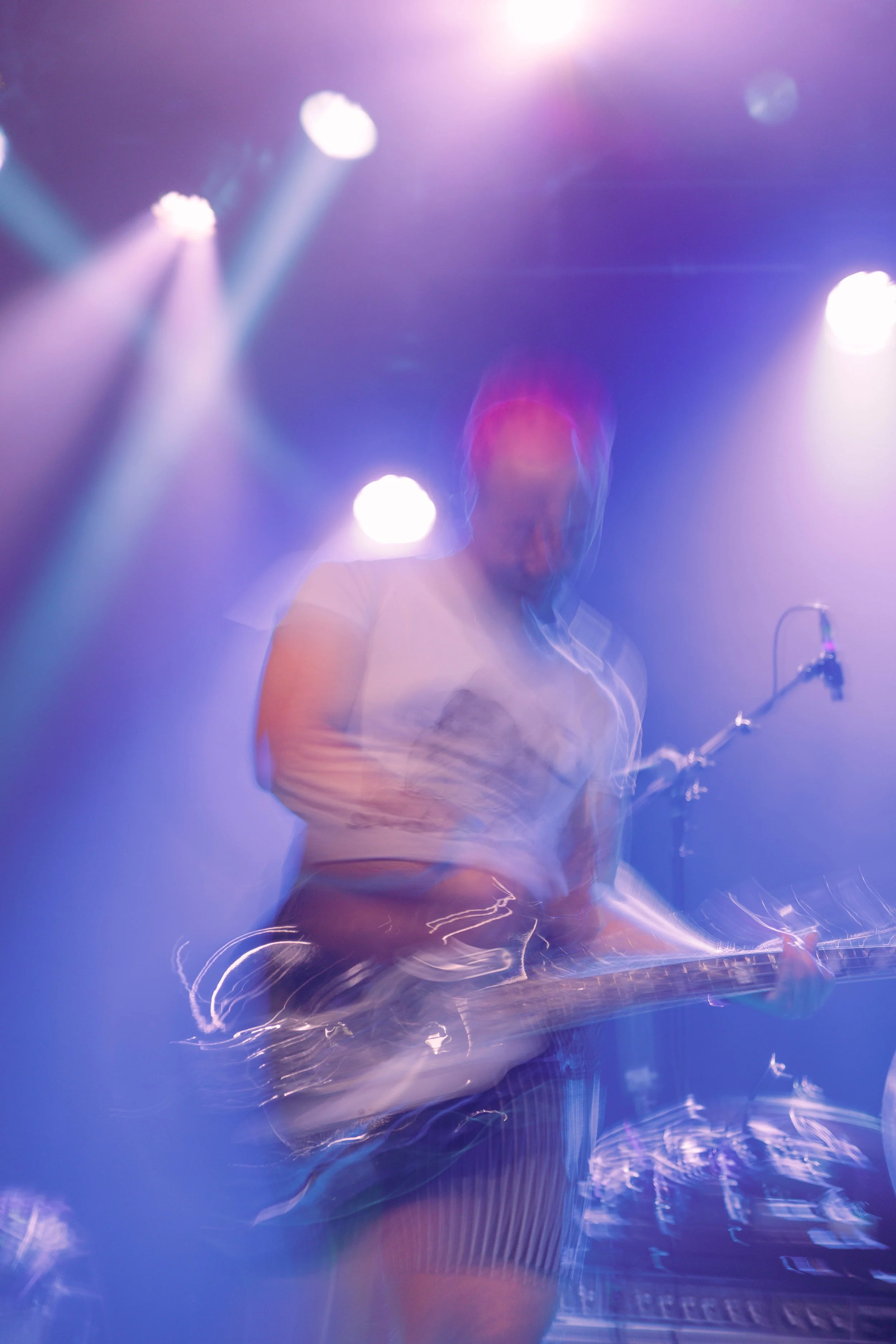 Blurred image of a person on stage illuminated by purple and blue concert lights, with a microphone stand nearby.