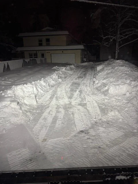snow-covered driveway with multiple tire tracks leading to a house at night.