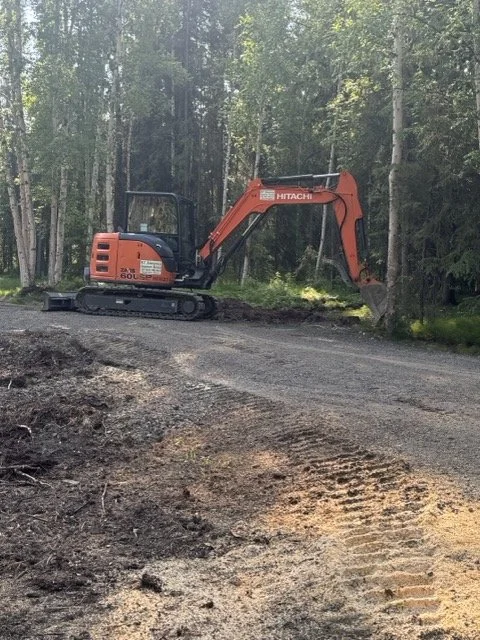 A small orange and black excavator working on a dirt path in a forested area.