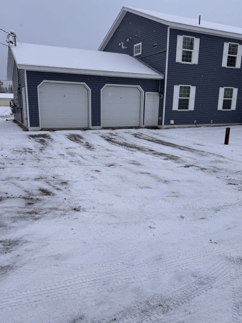 A blue house with a two-car garage covered in snow, with tire tracks visible on the driveway.