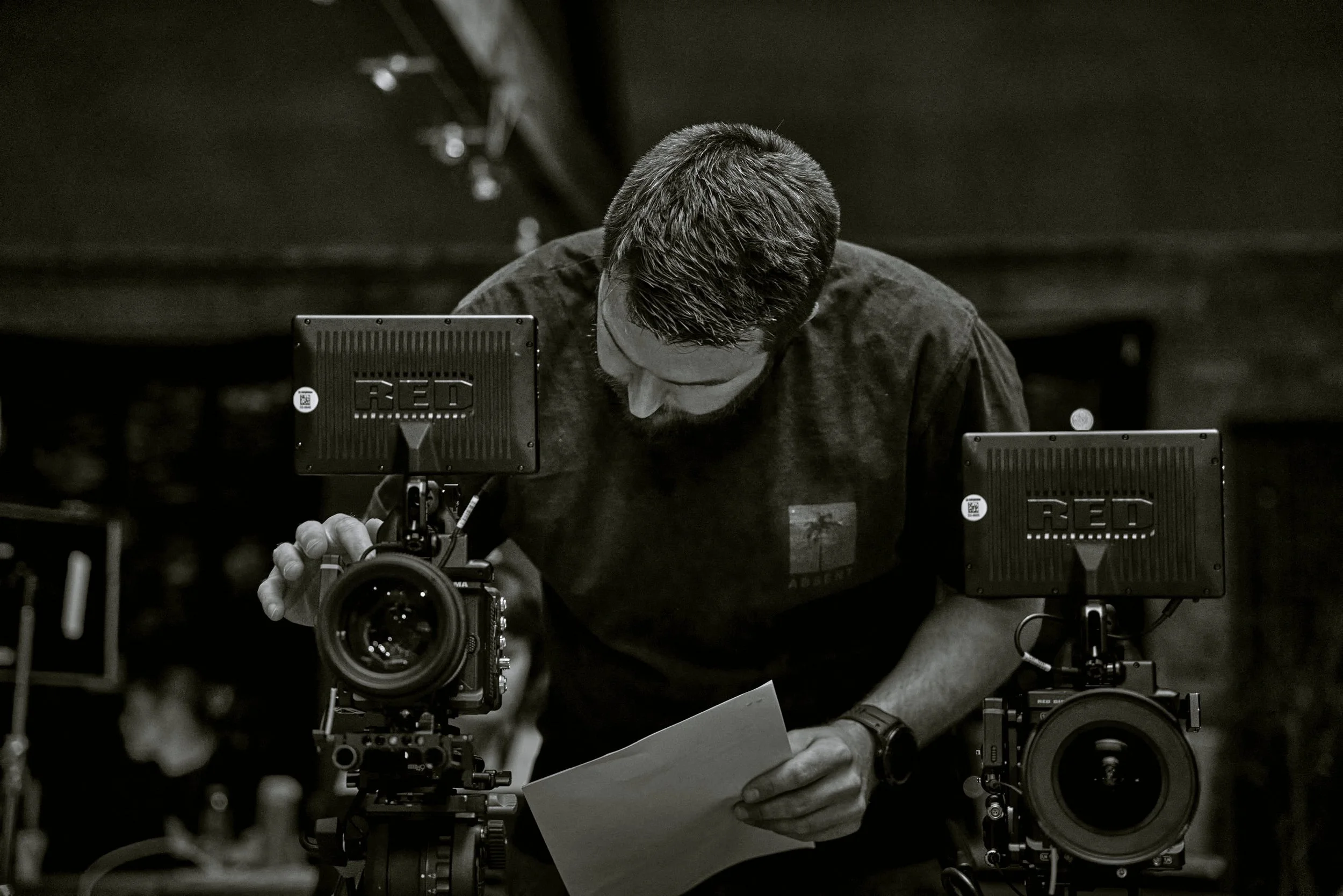 A man is preparing to shoot with a professional camera mounted on a stabilizer, surrounded by other camera equipment, in a dimly lit setting.