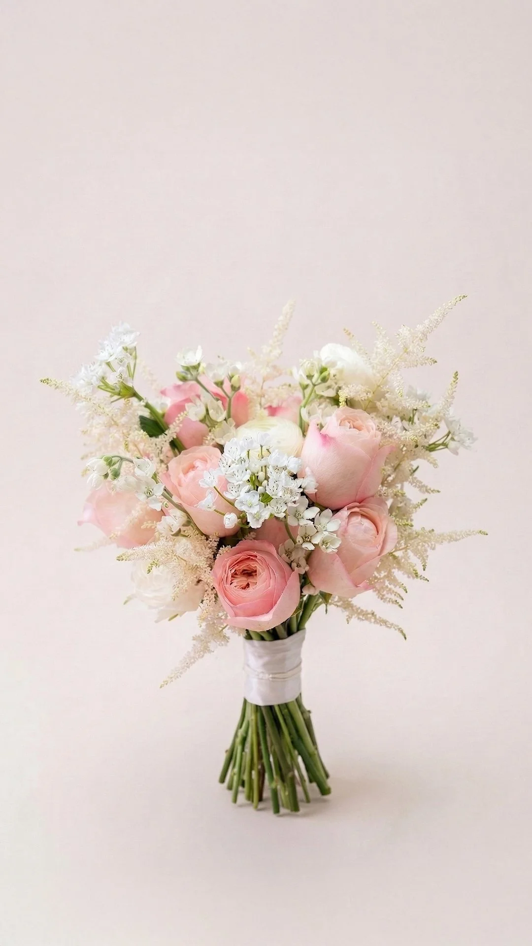 A bouquet of pale pink roses, white flowers, and greenery tied with a white ribbon.