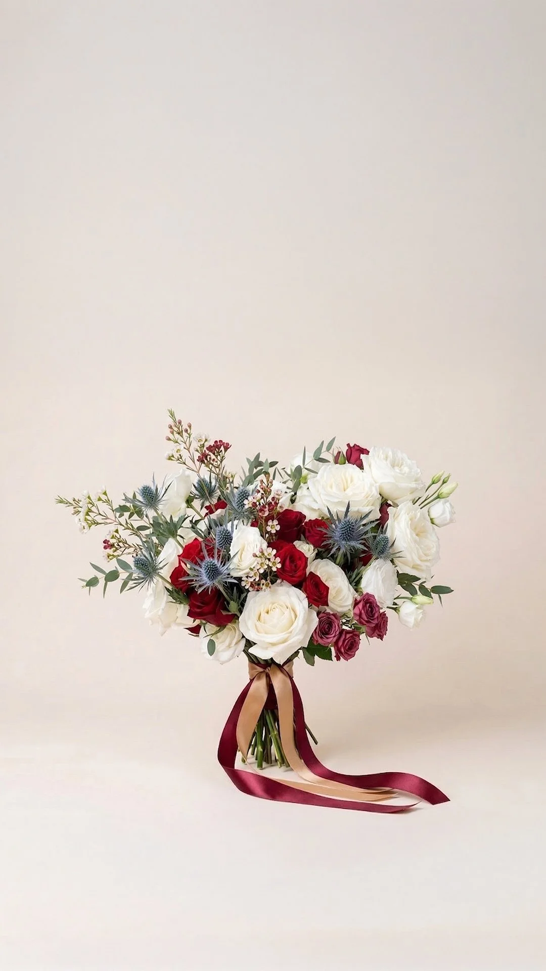 A bouquet of white, red, and purple flowers with greenery and long satin ribbons, set against a plain light background.
