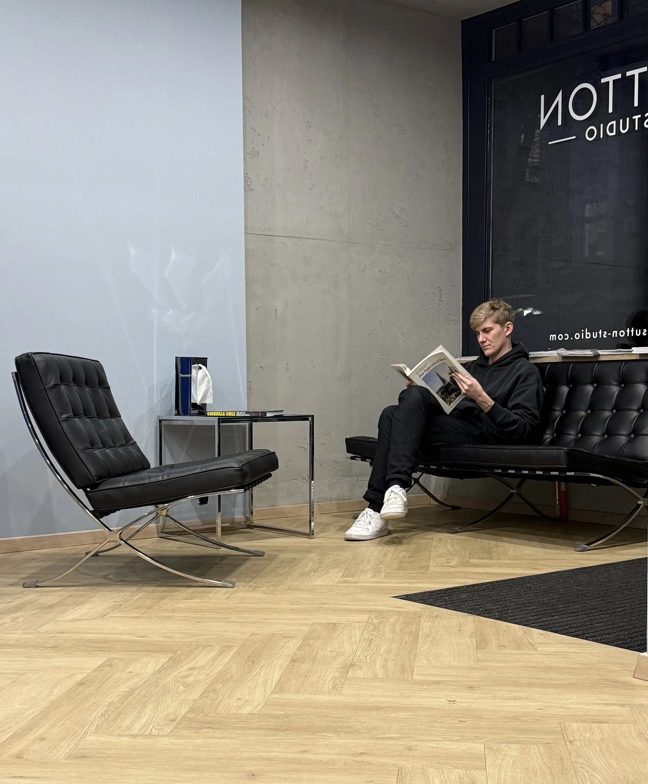 Ein junger Mann sitzt auf einer schwarzen Leder-Couch und liest ein Magazin in der modernen Lobby des Sutton Studio.