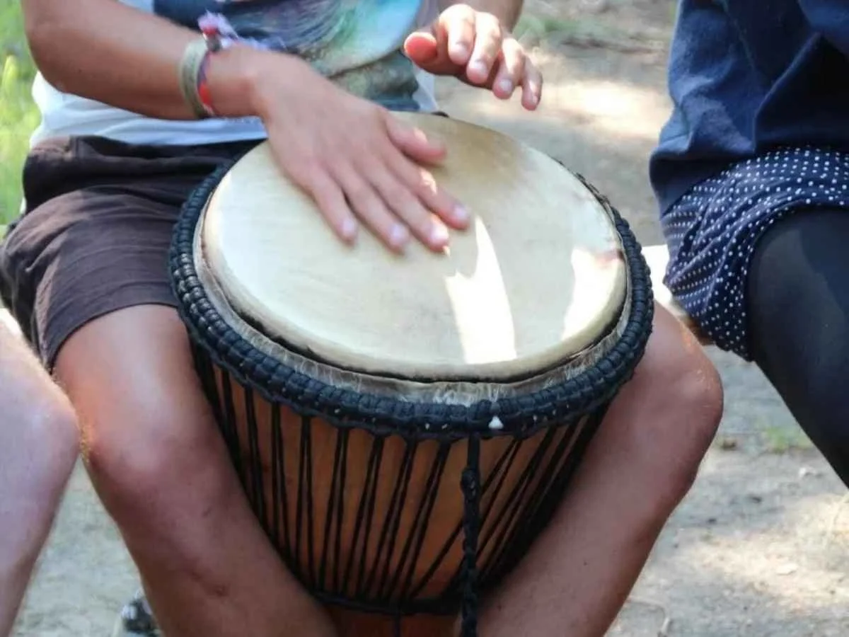 Close-up of a person's hands playing a traditional djembe drum during a Latin American rhythm session outdoors.