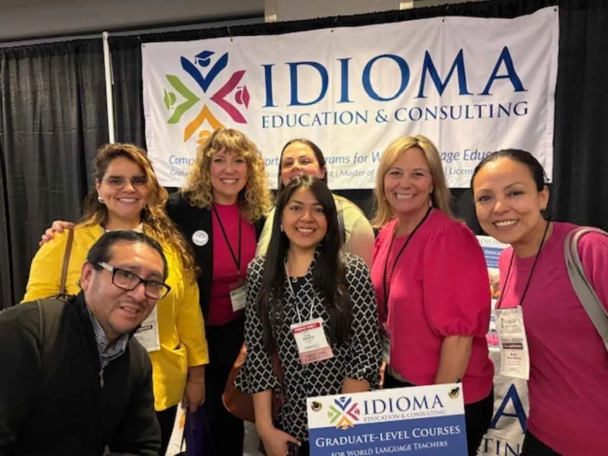 A group of six smiling educators, including members of the New Jersey Alternate Route program, posing together in front of an Idioma Education & Consulting banner at the NECTFL conference in Midtown Manhattan.