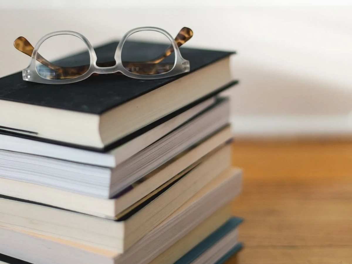 A pair of clear-rimmed glasses resting on top of a stack of academic books.