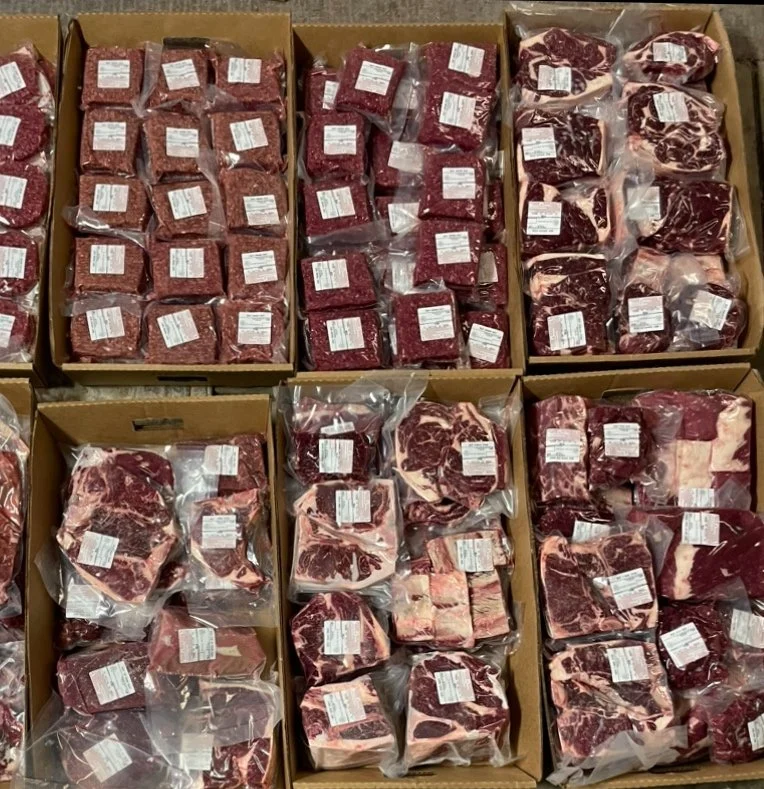 Various cuts of packaged beef and ground meat in cardboard boxes.