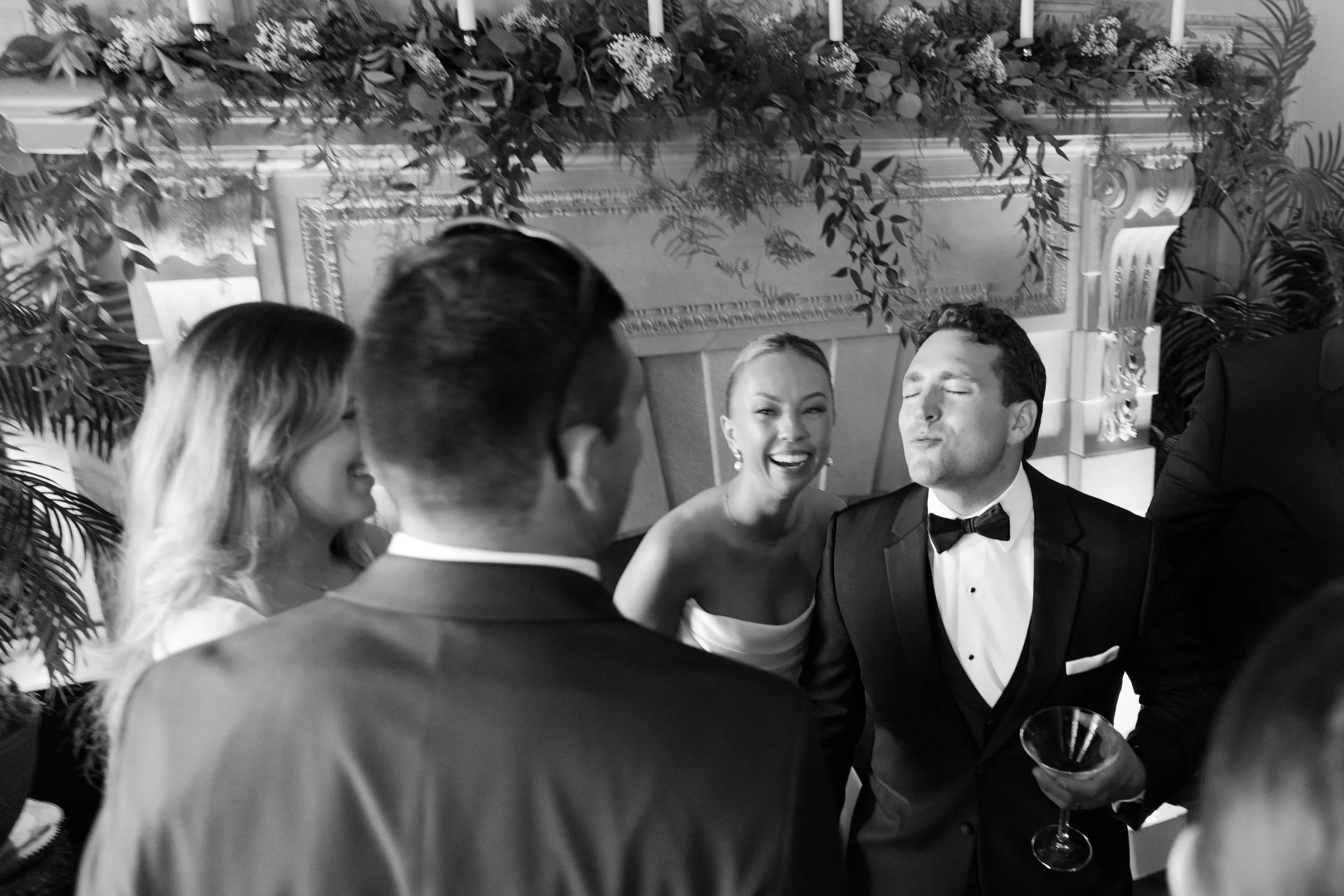 Group of people dressed in formal attire at a celebration, with a woman smiling and a man in a tuxedo holding a martini glass.