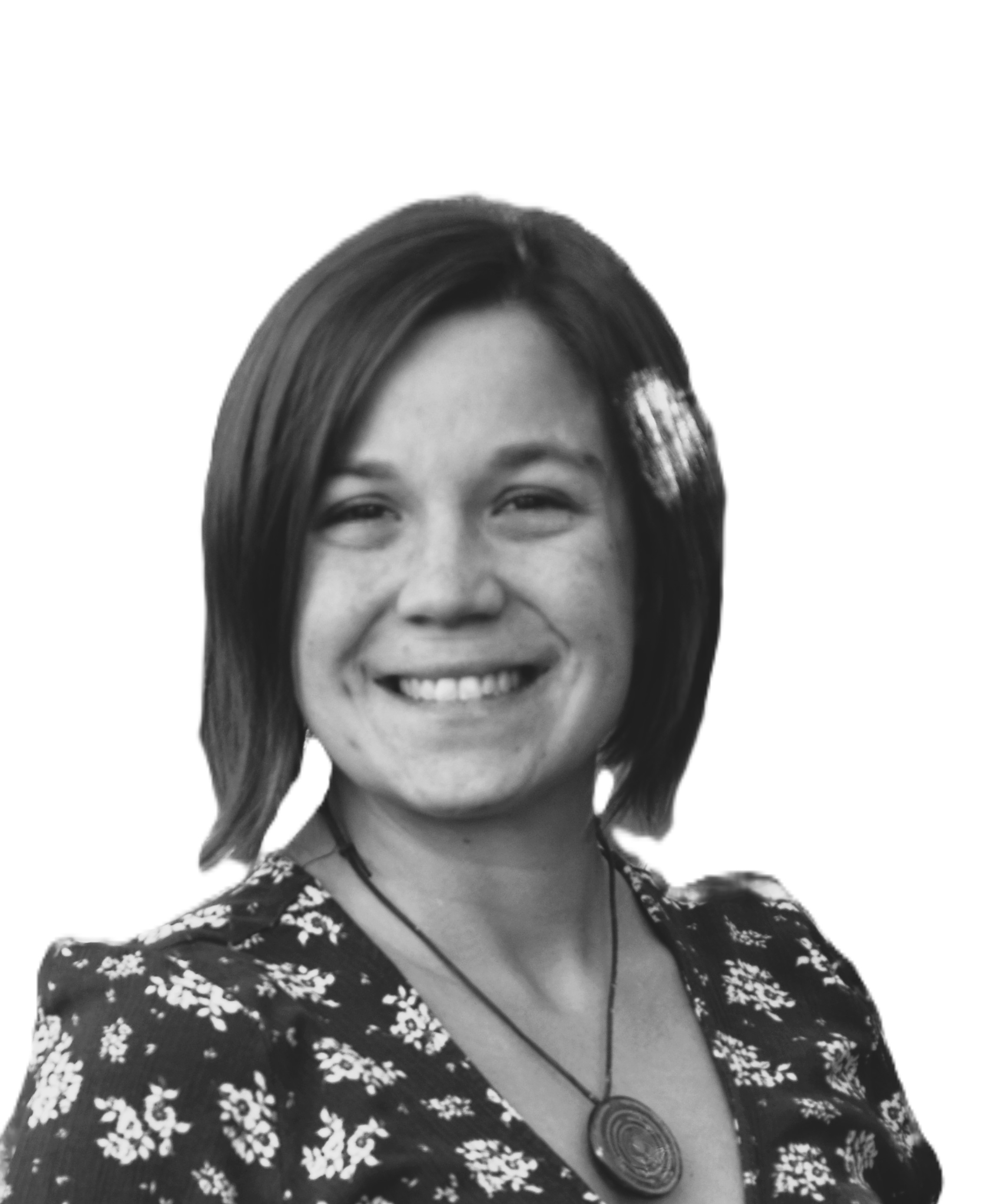Black and white photo of a smiling woman with shoulder-length dark hair wearing a floral patterned top and a large circular pendant necklace.