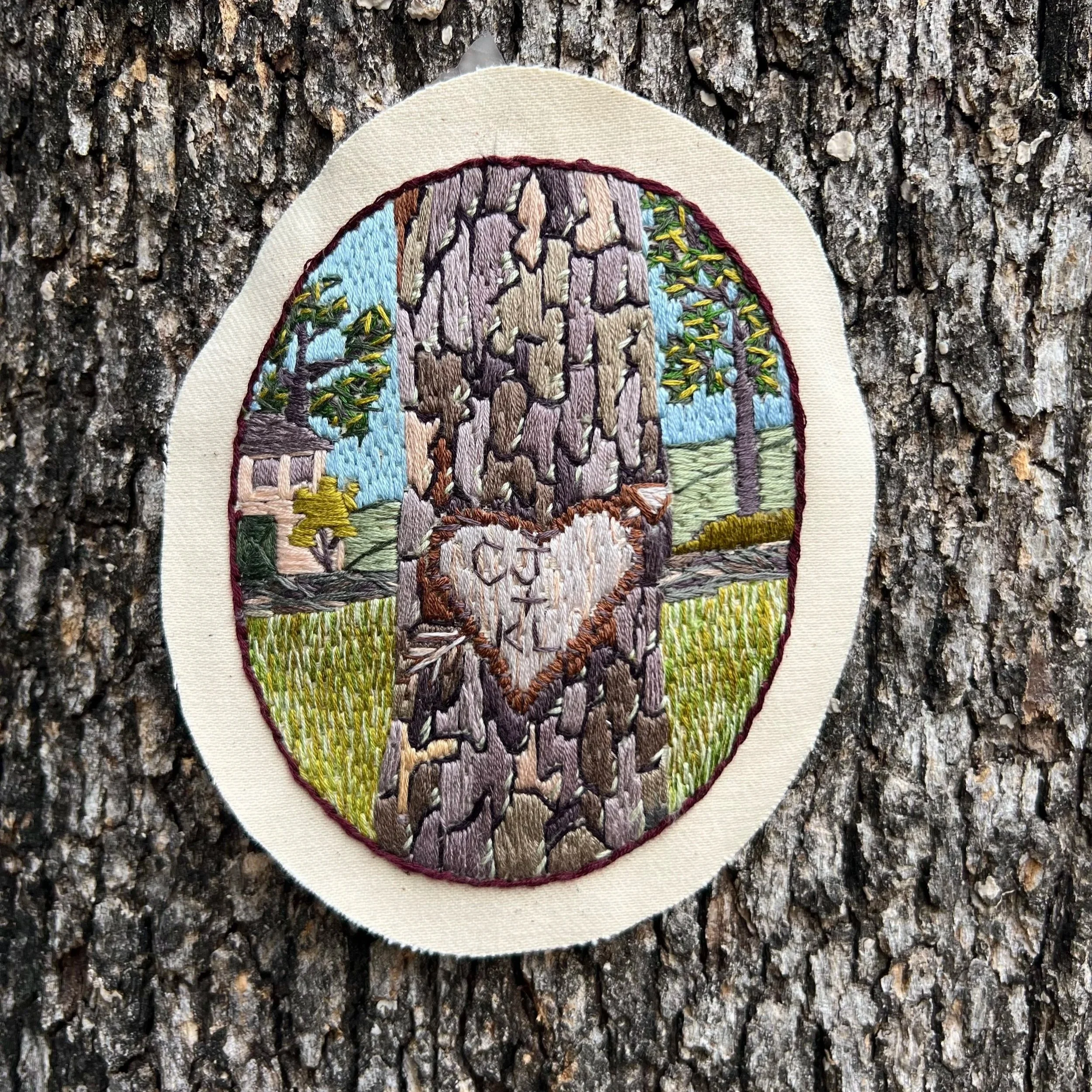Arbor Glyph hand-embroidered patch photographed against real tree bark, inspired by carved initials and the act of marking memory in the world.