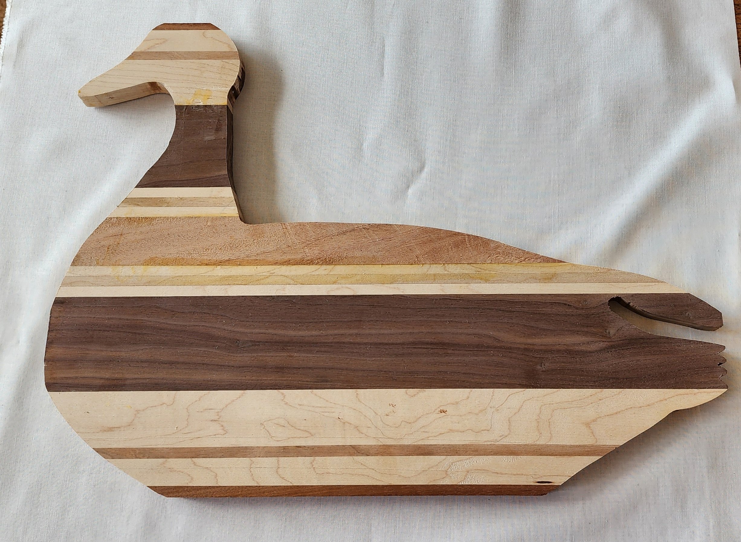 A wooden cutting board shaped like a dachshund dog, made of different wood tones.
