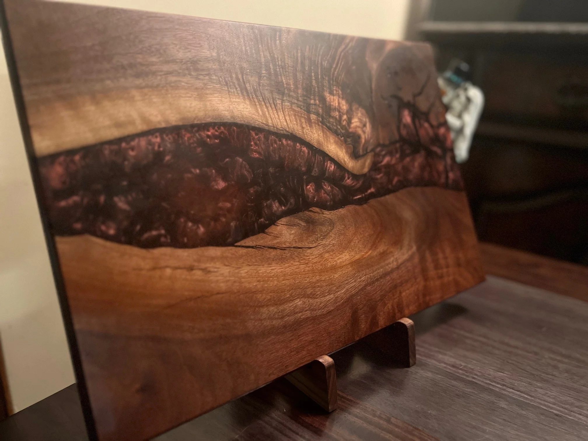 A wooden art piece with a natural wood finish and a dark, textured inlay in the center, displayed on a wooden stand.