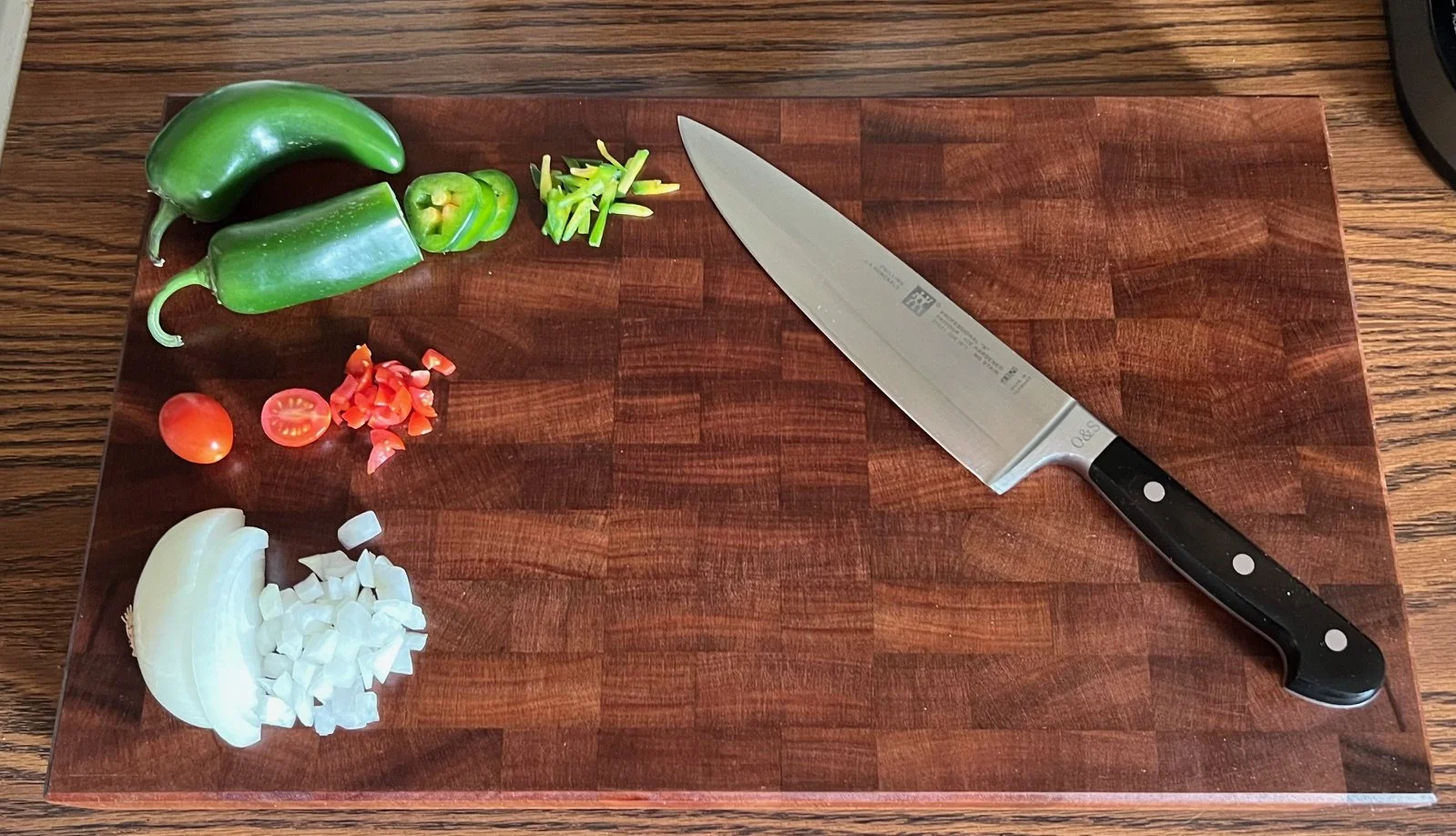 Chopping board with peppers, cherry tomatoes, onions, and garlic, with a large chef's knife.