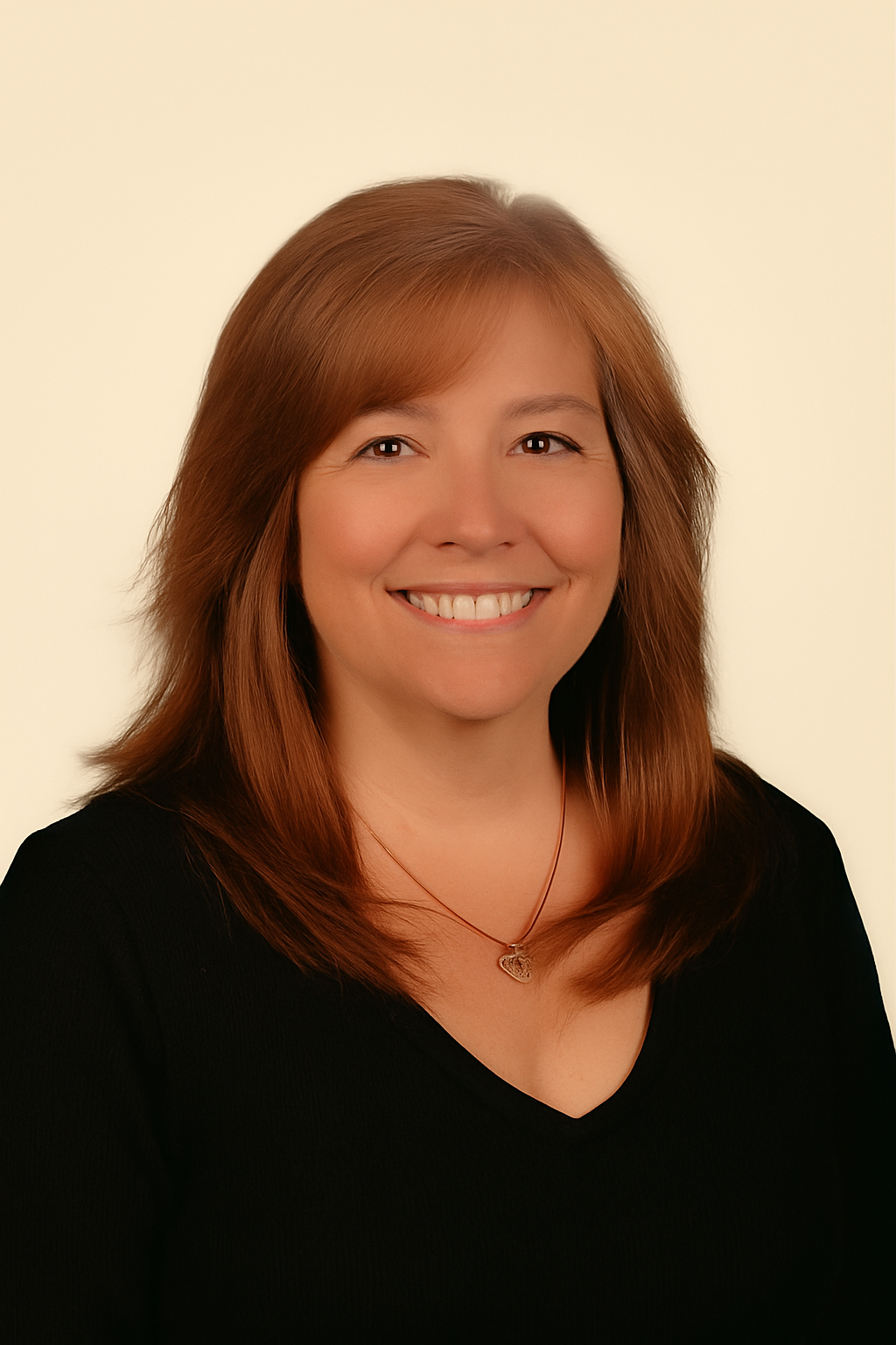 Headshot of a woman with long, reddish-brown hair smiling, wearing a black top and a gold necklace with a heart-shaped pendant against a plain light background.