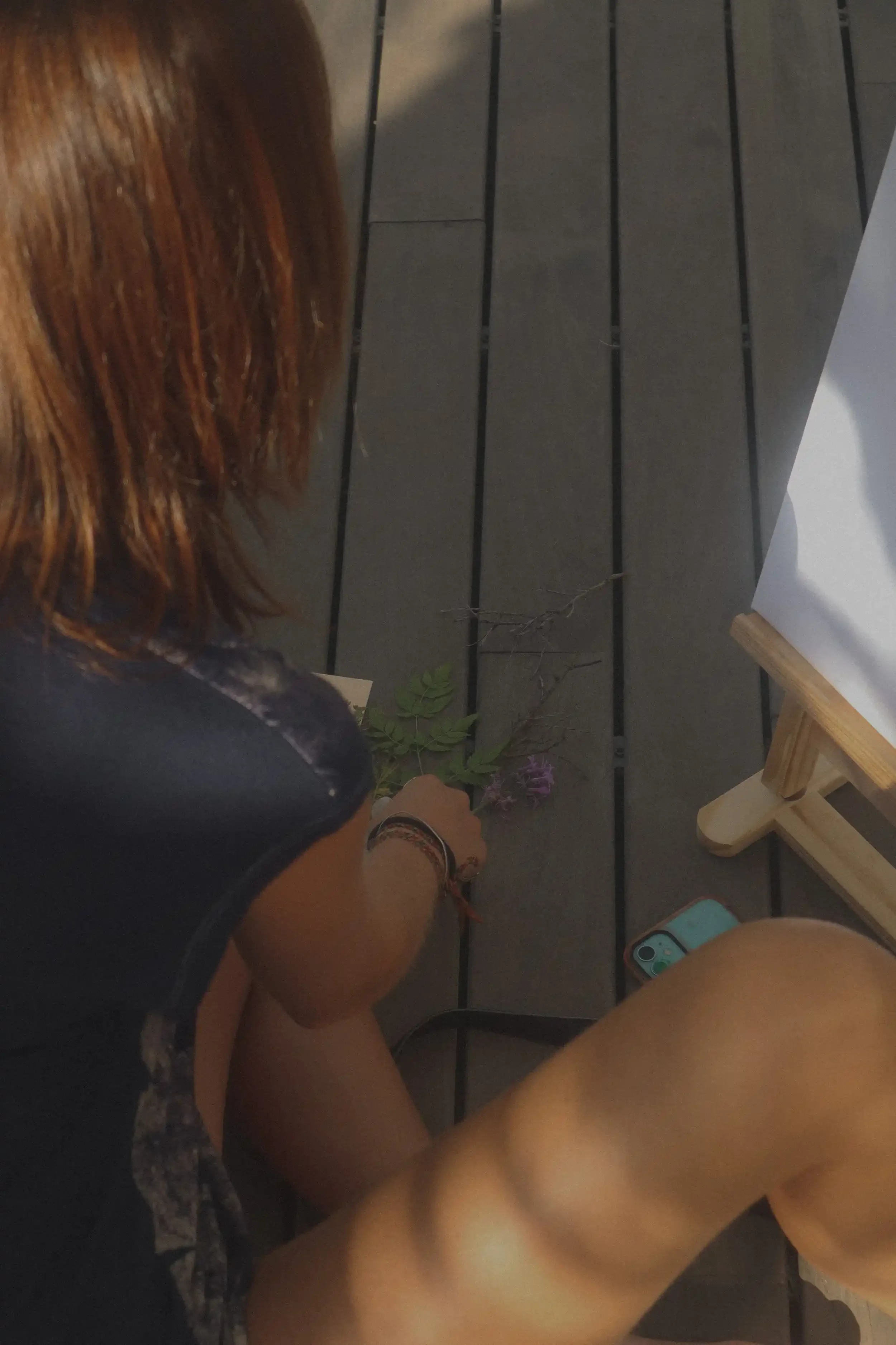 Persona arreglando flores sobre un piso de madera al lado de un caballete y un teléfono móvil.