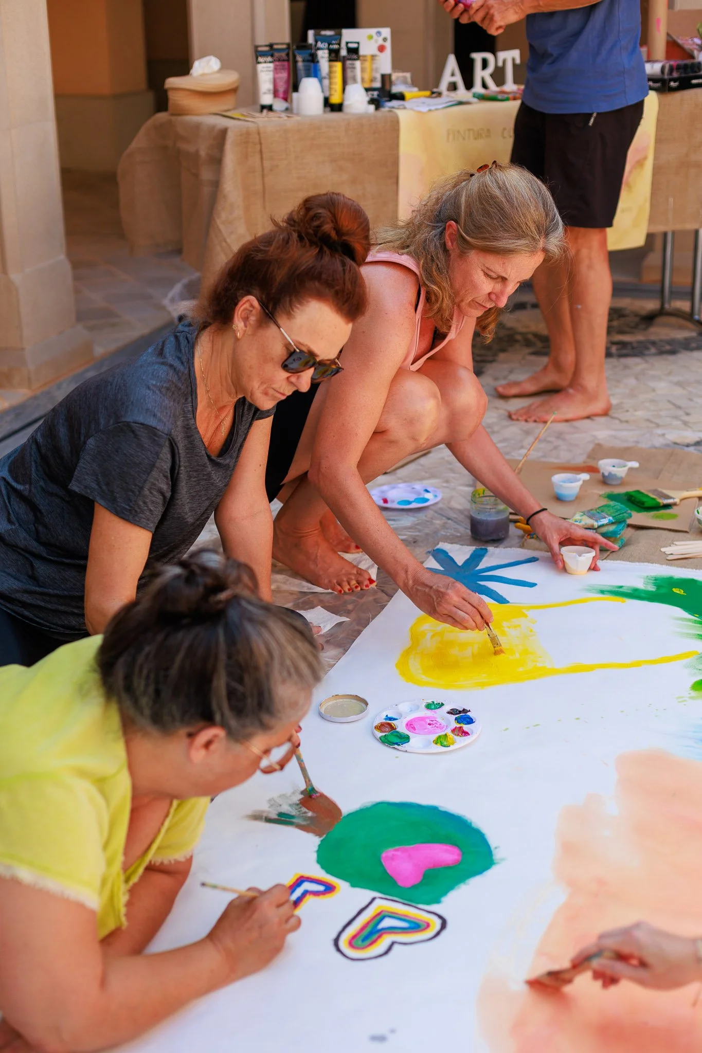People painting a large colorful mural on the floor, with art supplies around them.