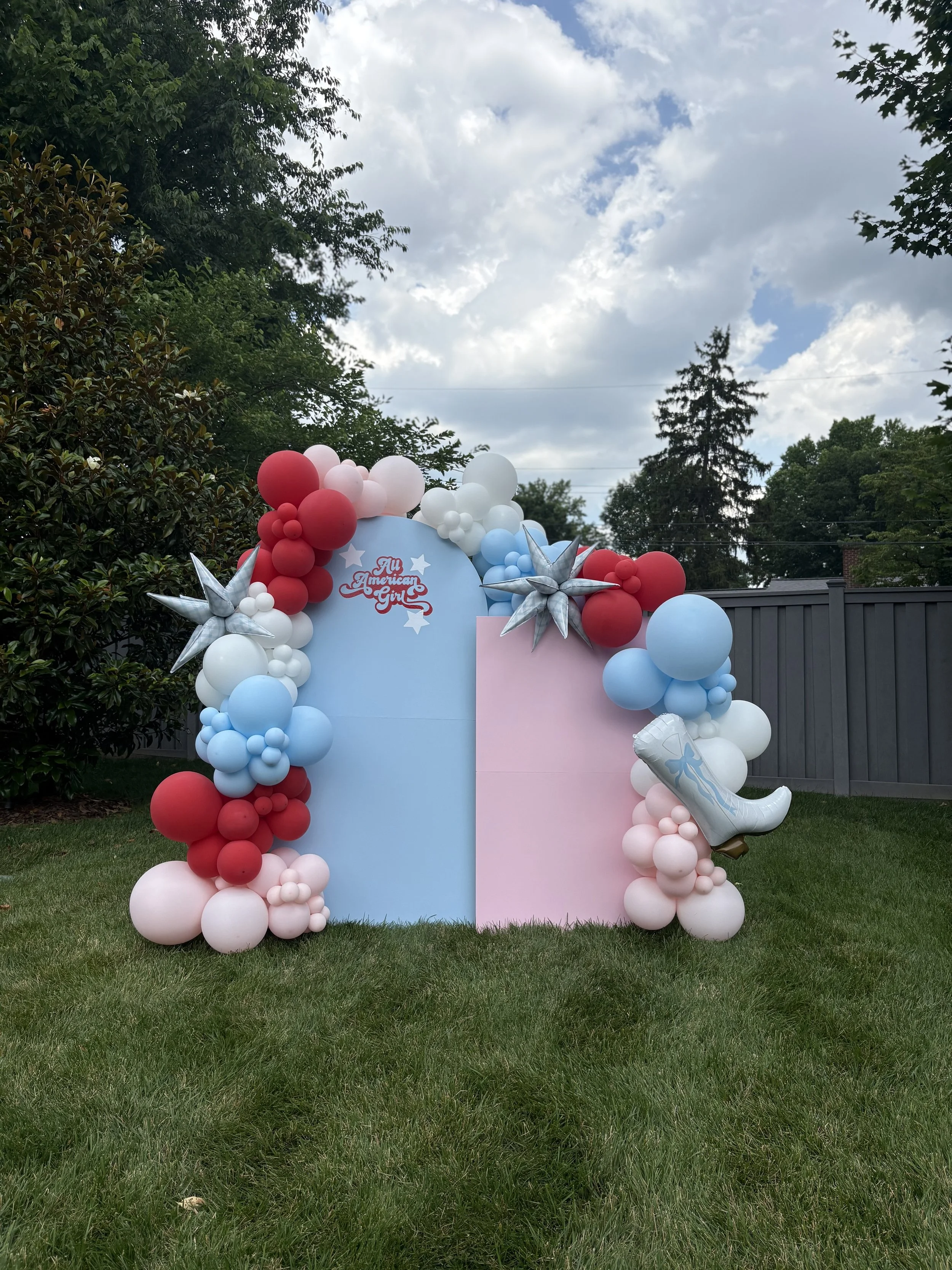 Decorative balloon setup with black, white, and gold balloons around a white backdrop with the words 'The Night Before' printed on it, likely for a celebration or event.