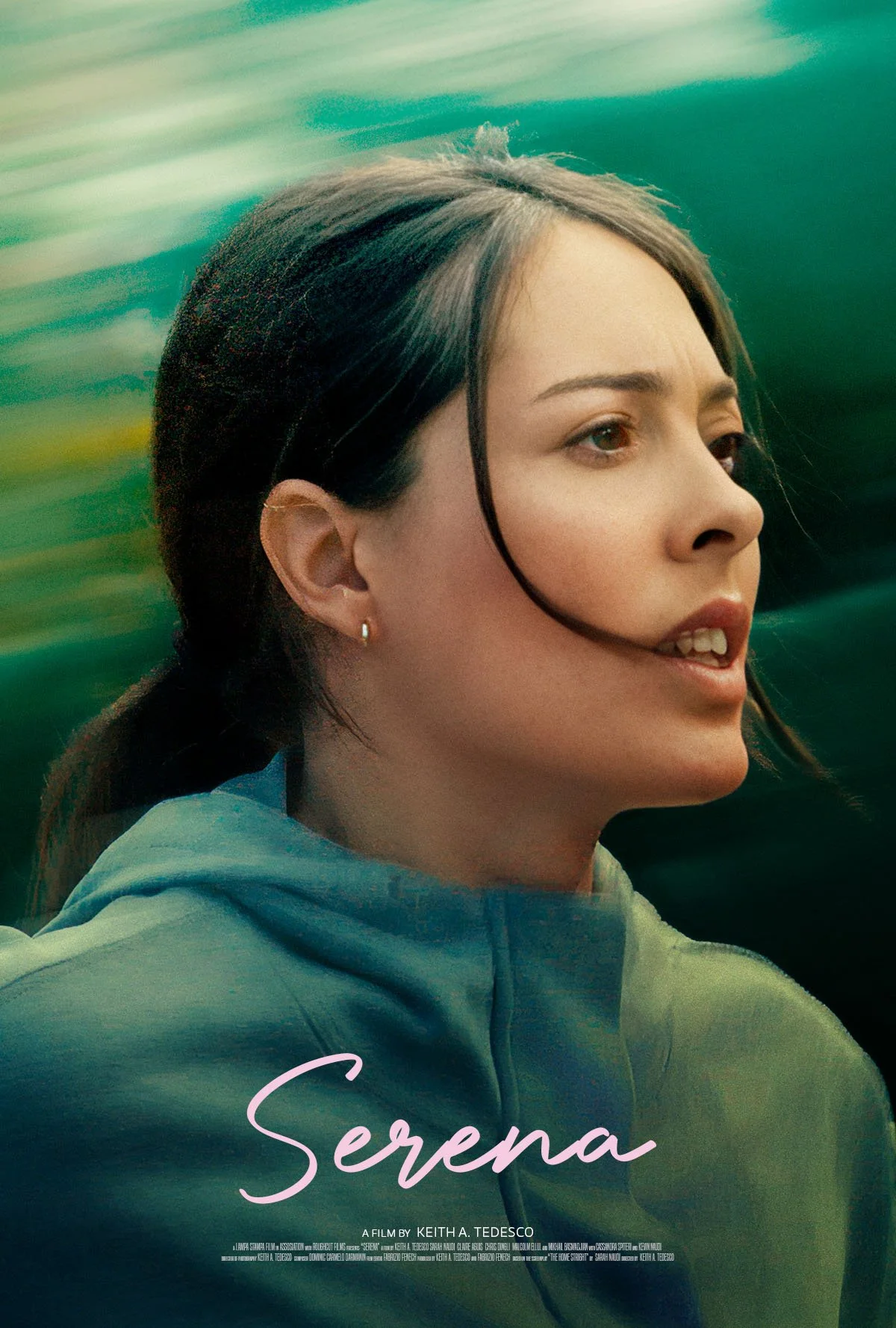 Close-up of a woman with dark hair pulled back, wearing a green jacket, looking to the side with a blurred green background.