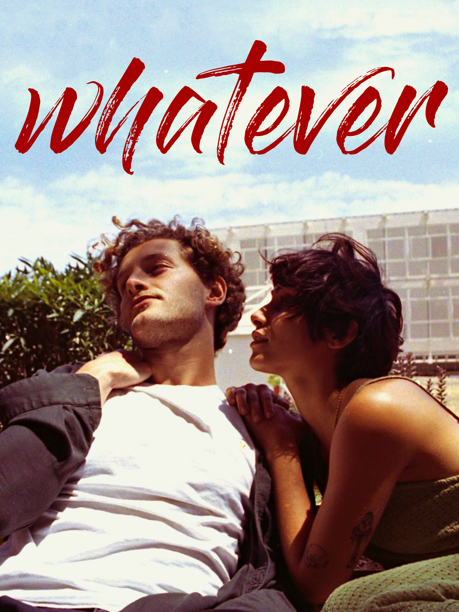 Two young adults sitting outside on a sunny day. The man has curly hair, and the woman has short dark hair. They are close to each other, with the woman touching the man's shoulder. The background shows a building and greenery, and the sky is clear. 