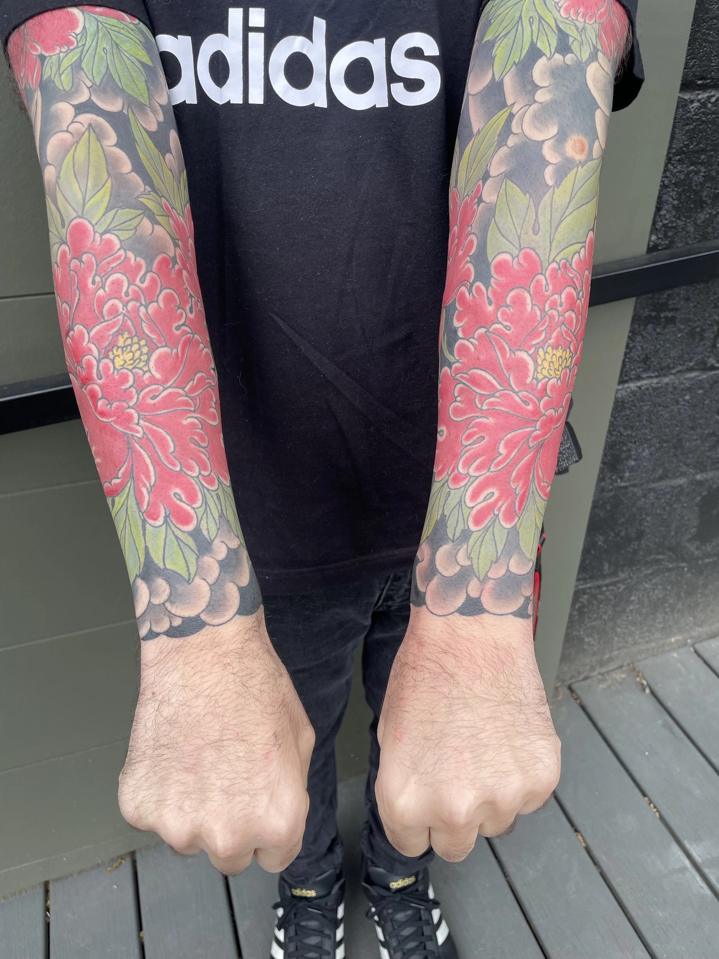 Person with colorful Japanese peony tattoos with green leaves and traditional Japanese background