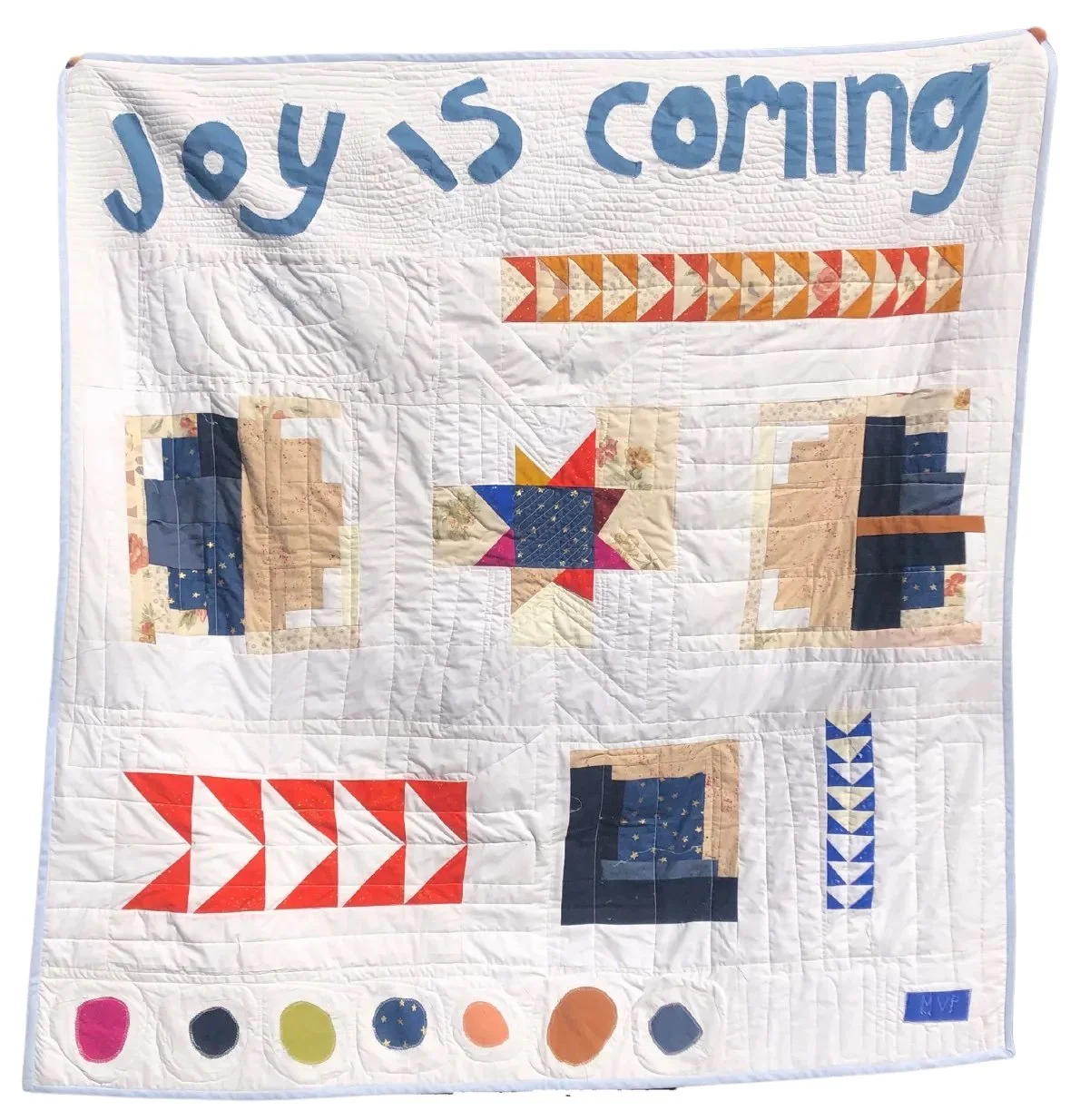 white quilt with log cabins, flying geese, appliqued blobs, and the words "joy is coming" appliqued 