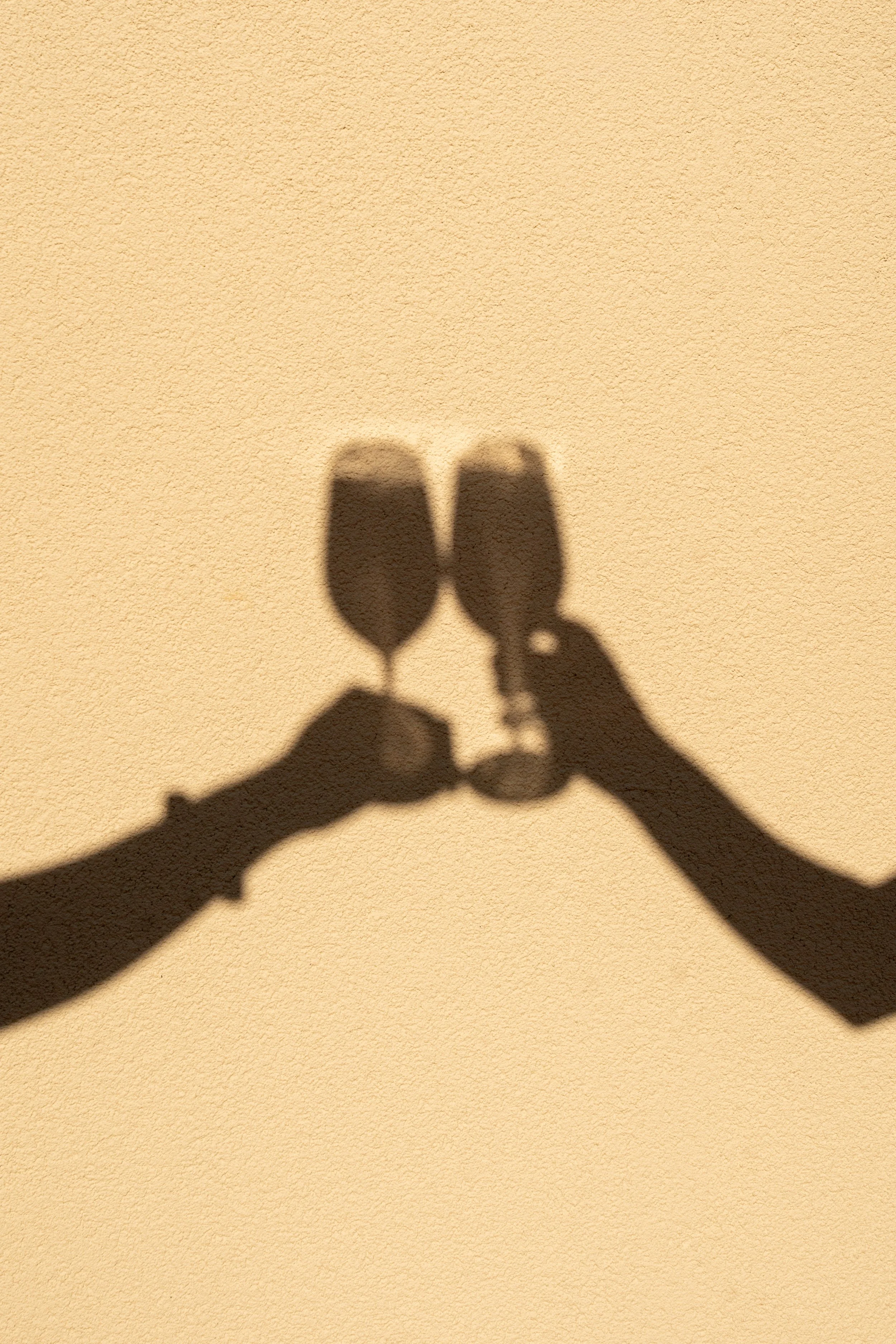 Shadow of two hands holding glasses on a textured yellow wall.