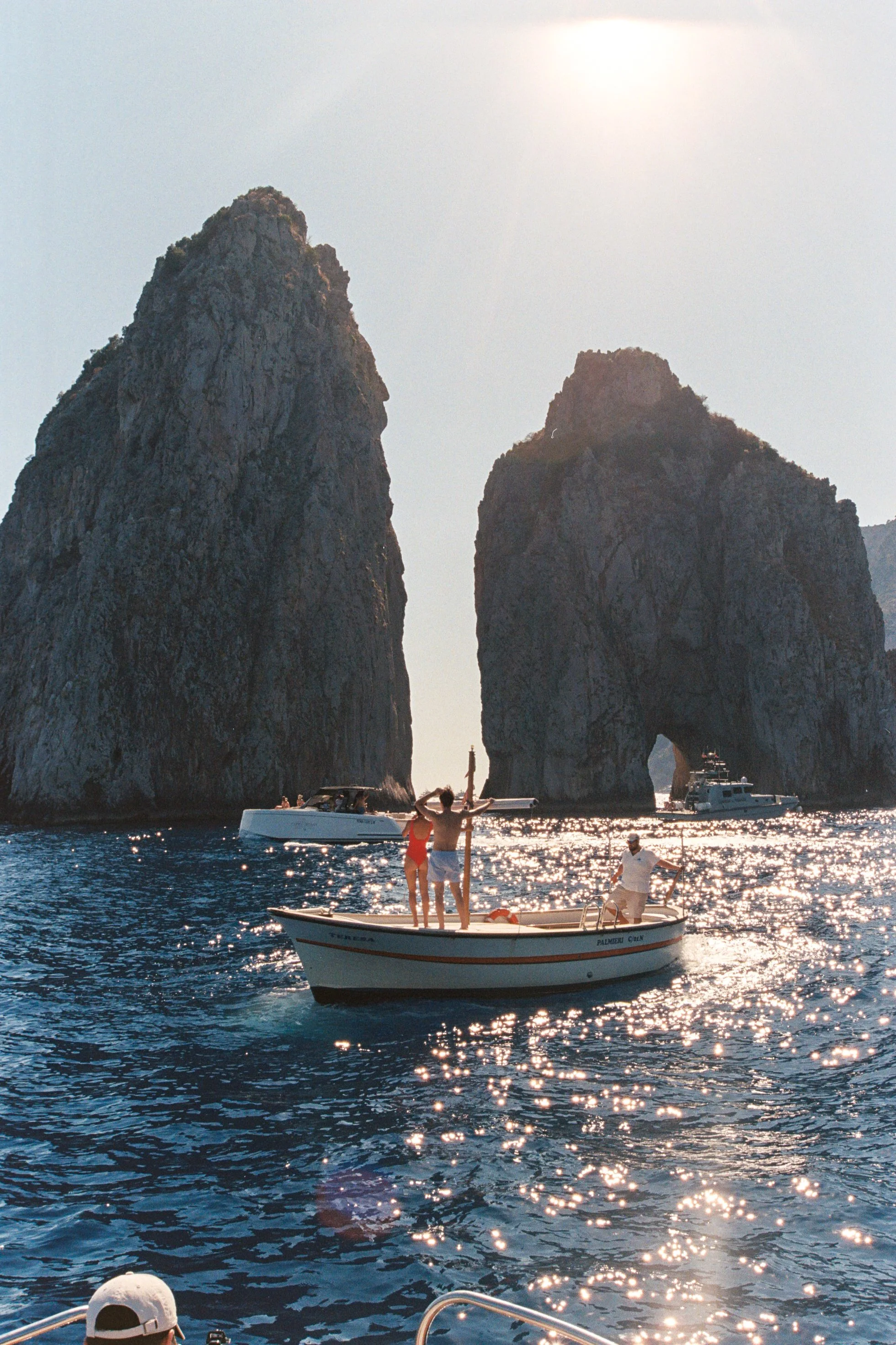 People enjoying a boat ride on the water near large rock formations with the sun shining.