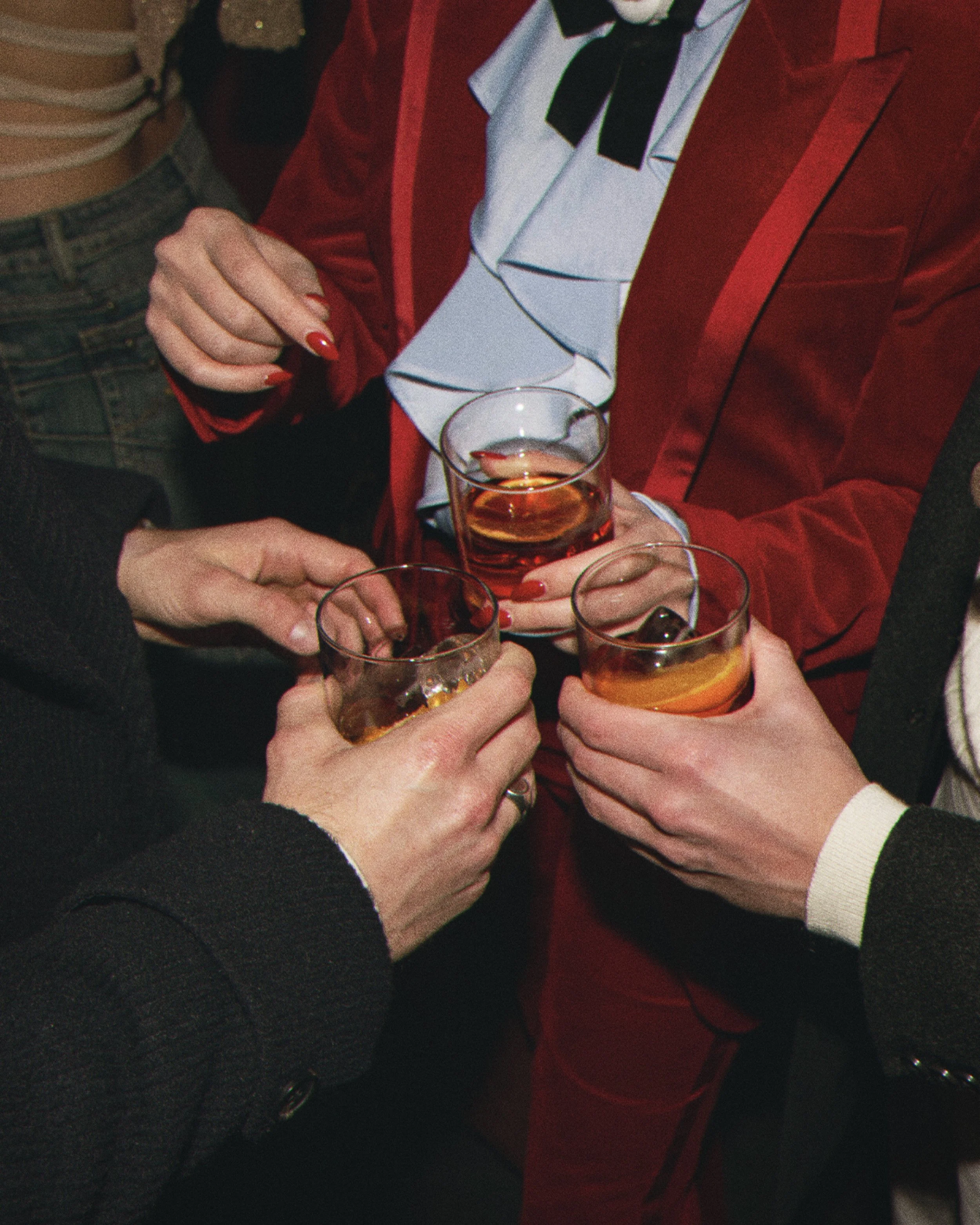 People holding glasses of beer, with some wearing formal attire and accessories indicating a social or celebratory gathering.