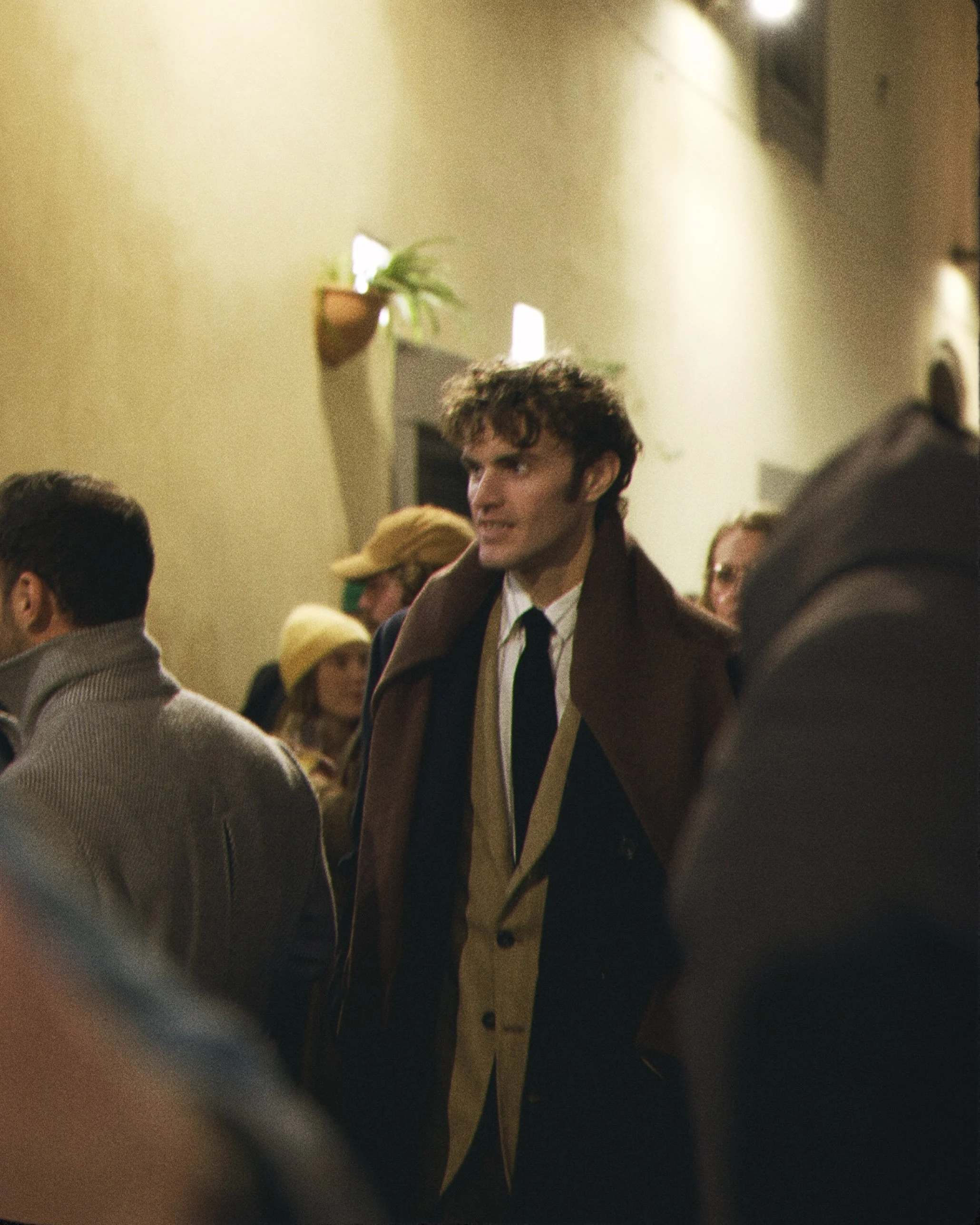 A person with a 1960s hairstyle and vintage clothing in a crowded indoor setting.