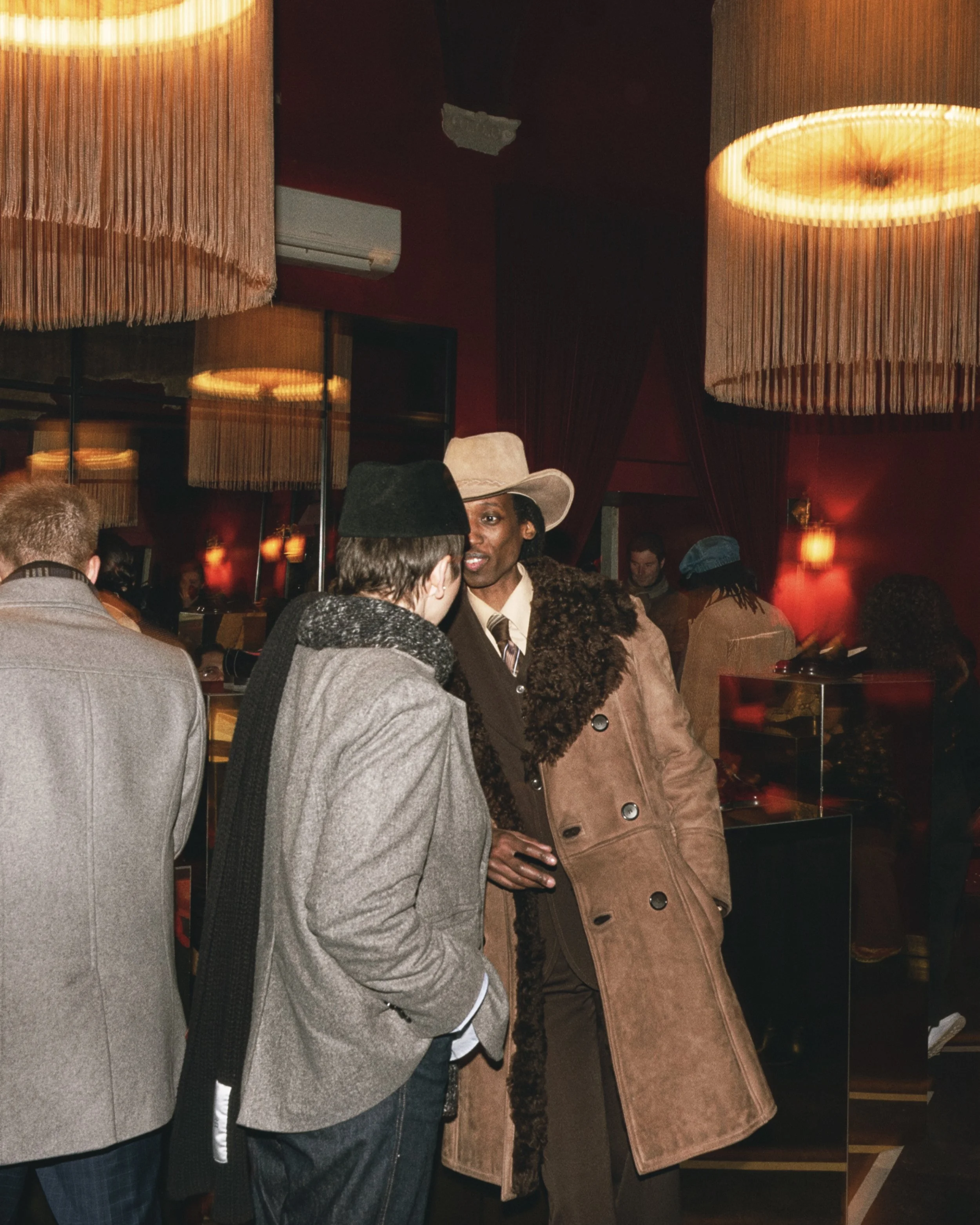 People gathered in a dimly lit room with hanging pendant lights, engaged in conversation.