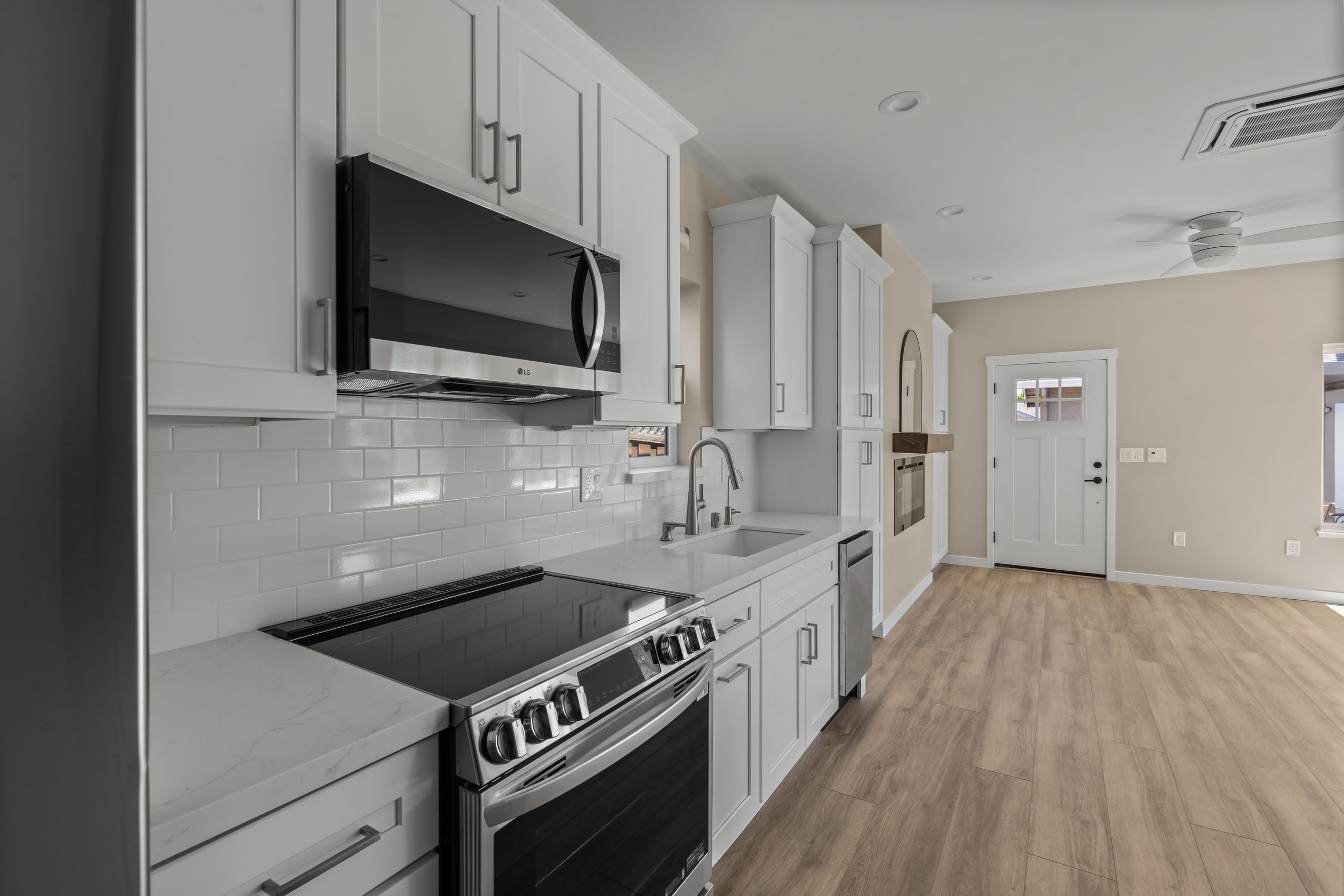 Modern kitchen with white cabinets, stainless steel microwave and oven, black stovetop, white subway tile backsplash, and light wood flooring.