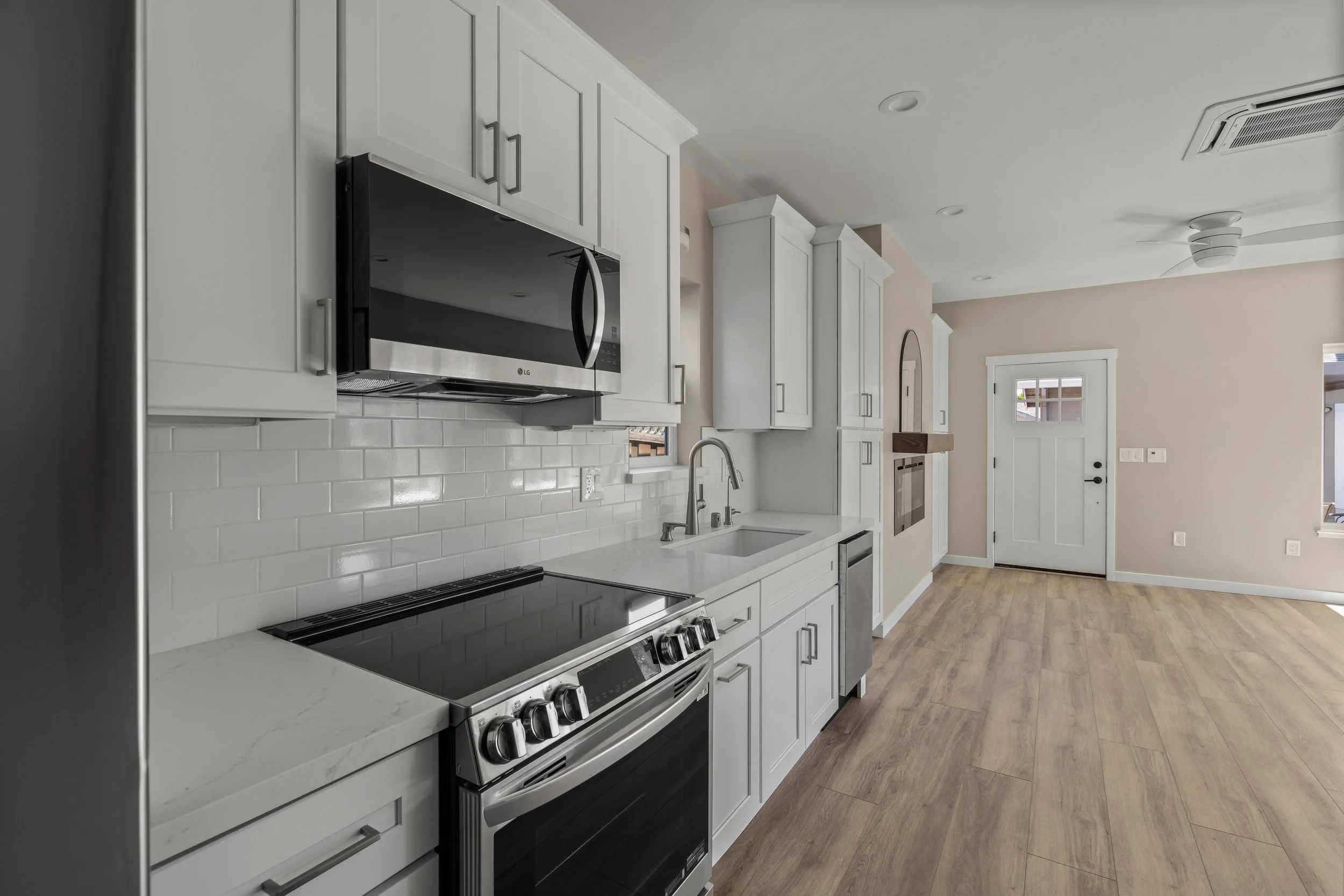 Modern kitchen with white cabinets, stainless steel microwave and oven, black electric stove, white subway tile backsplash, and wood flooring.