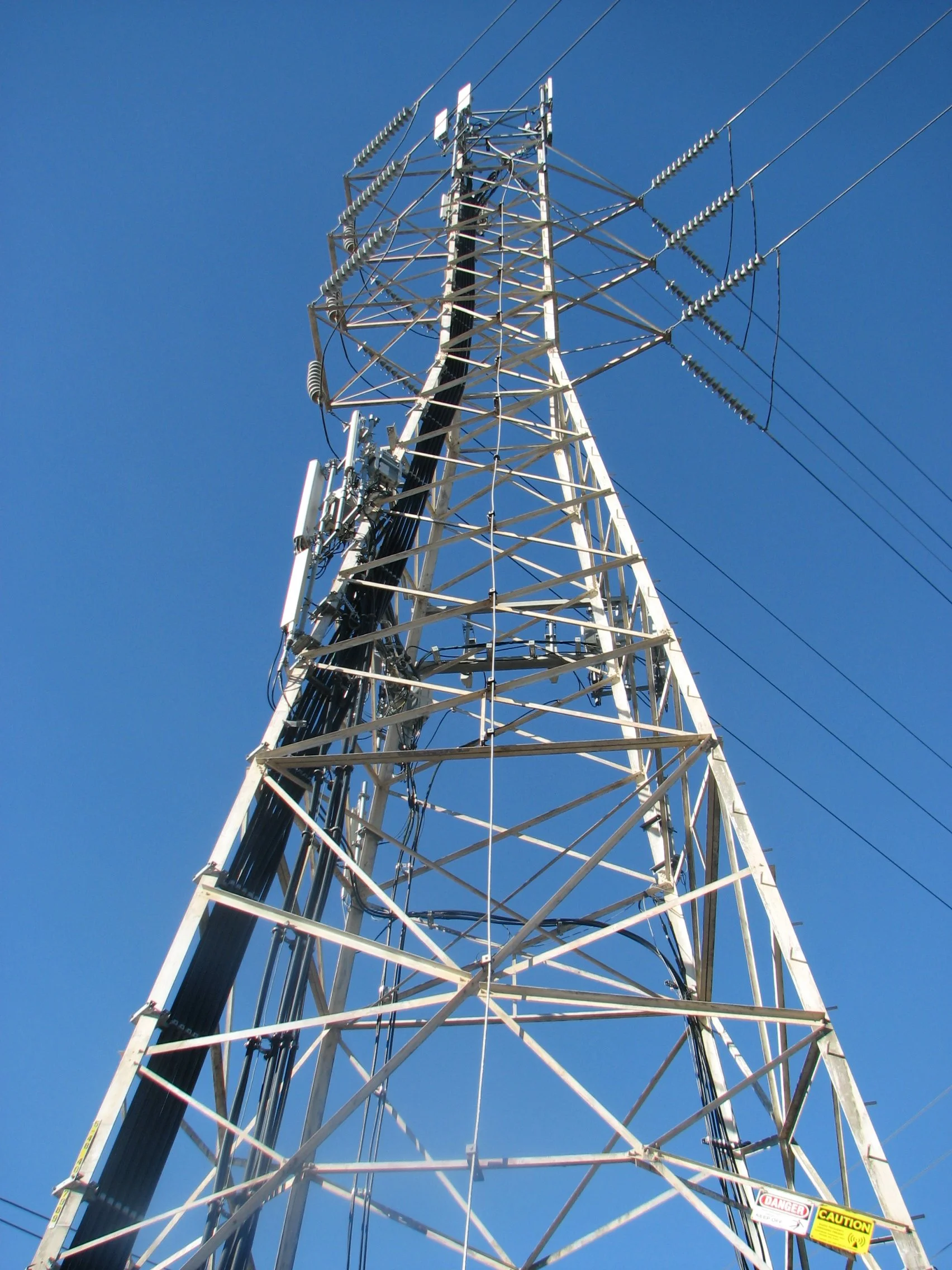 A tall metal communication tower with antennas and wires against a clear blue sky.