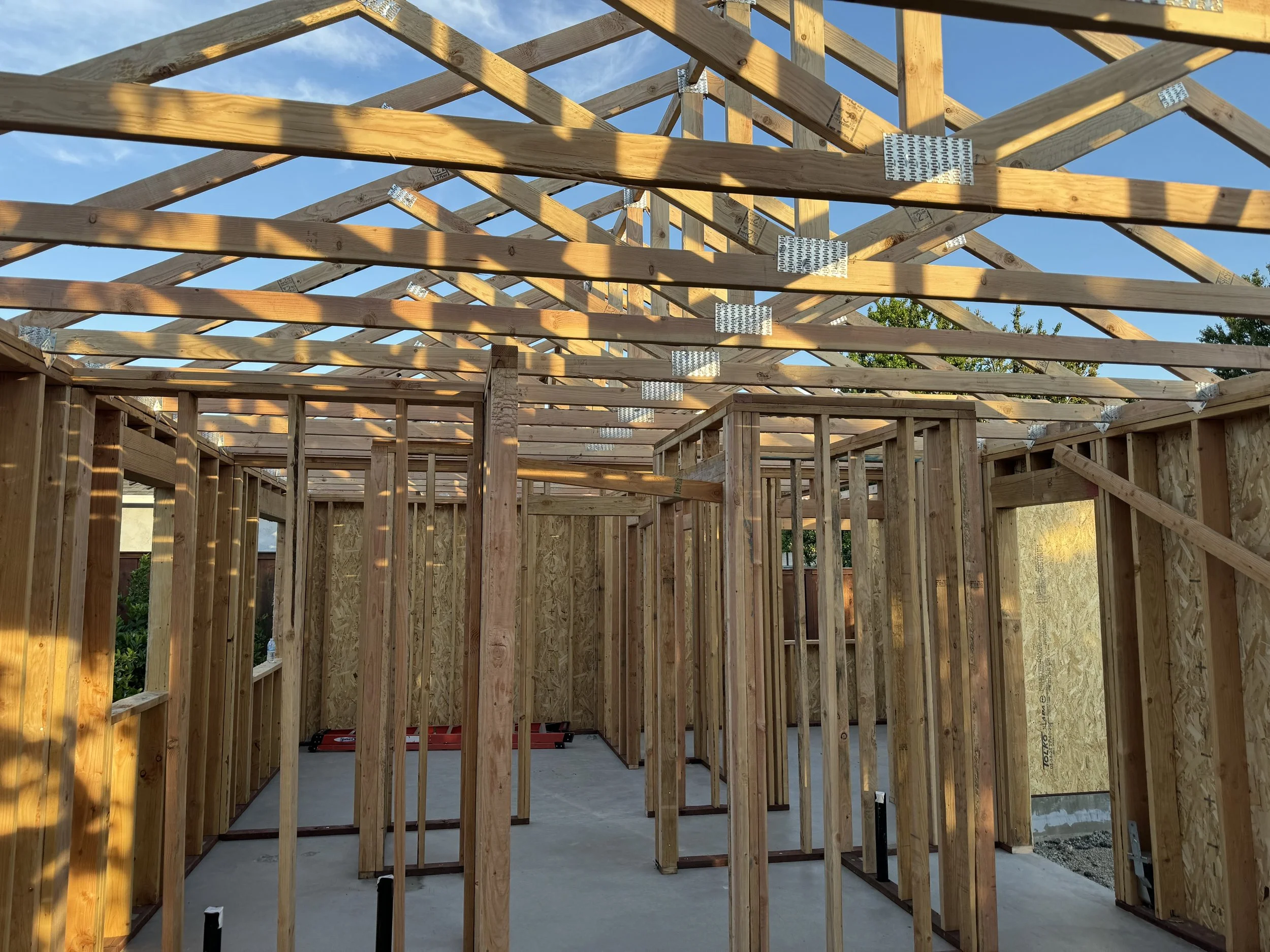 Wooden framing of a house under construction with visible roof trusses and interior wall studs.